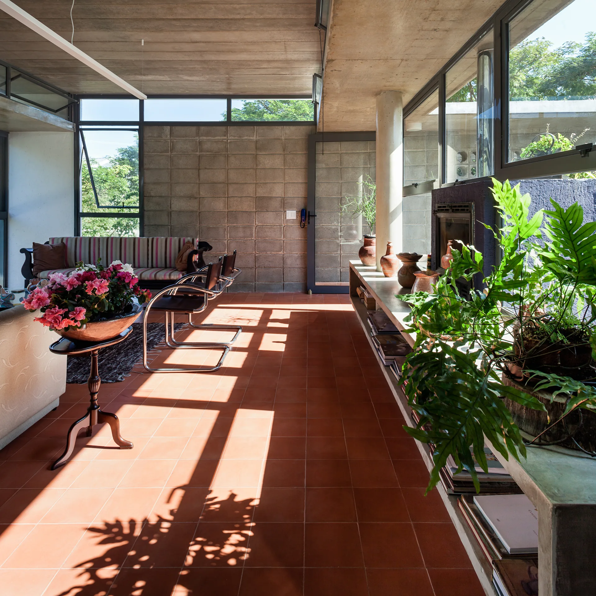 Sunlit modernist living room featuring terracotta tile flooring, exposed cinder block walls, a concrete ceiling, and a long built-in concrete shelf.