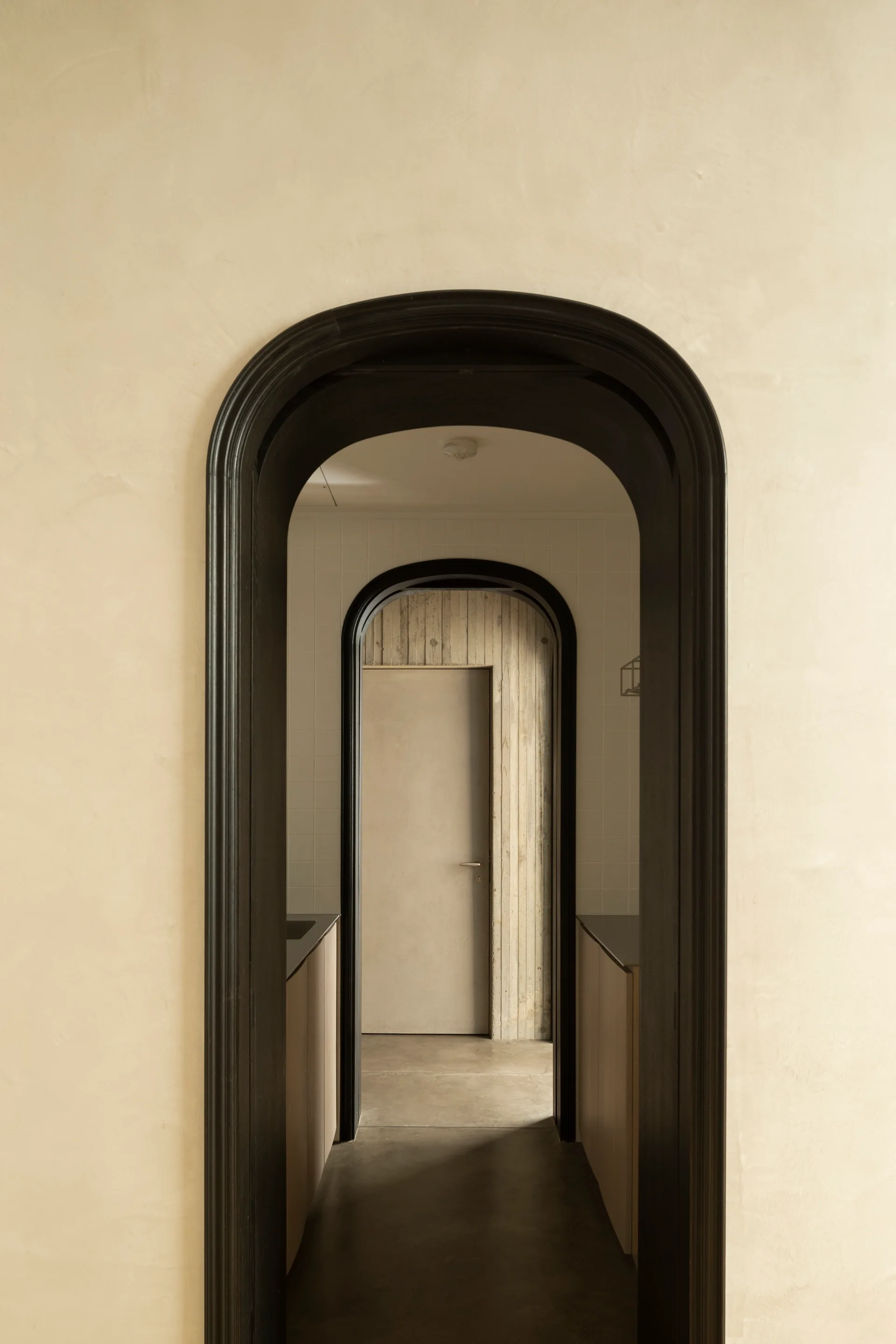 A view down a hallway through several nested arched doorways with prominent black casings and beige plaster walls.