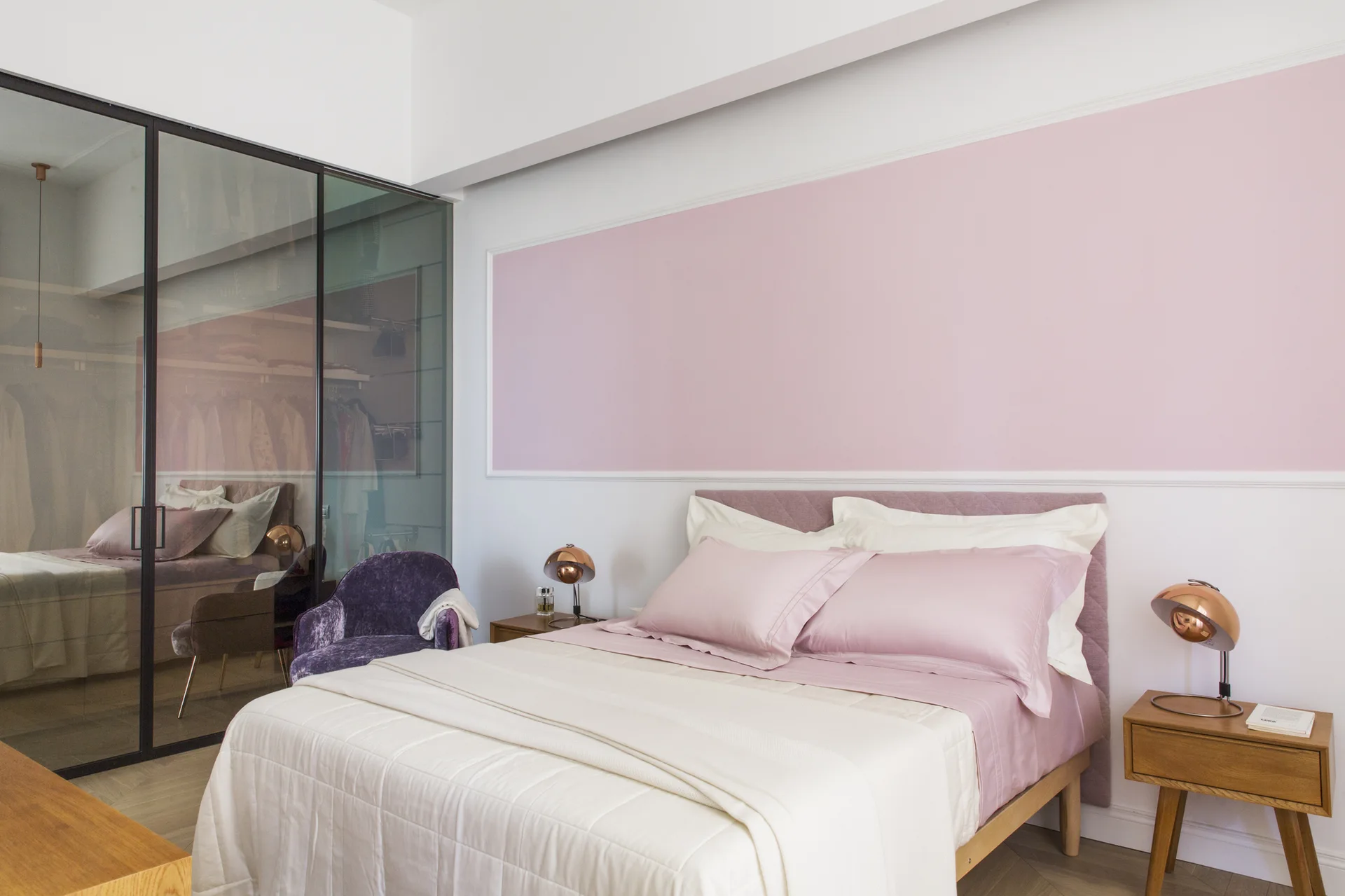 A modern bedroom featuring a bed with pink sheets, wooden nightstands with copper lamps, and a black-framed glass wardrobe.