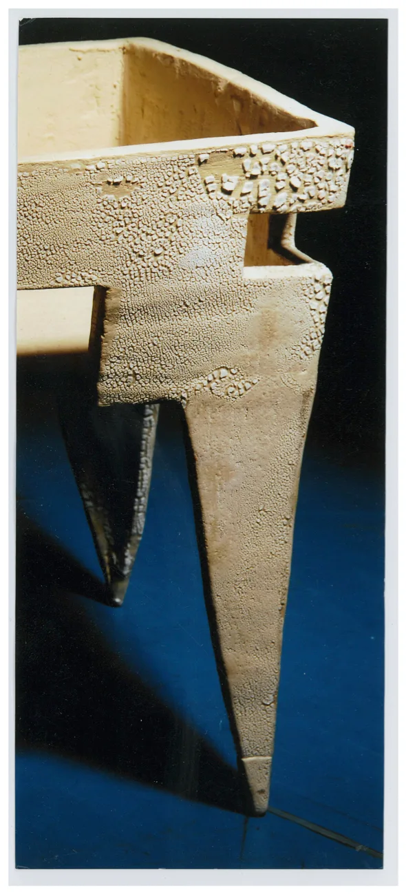 A cream-colored ceramic table featuring a heavily crackled surface and sharp tapered legs sits against a dark blue and black background.
