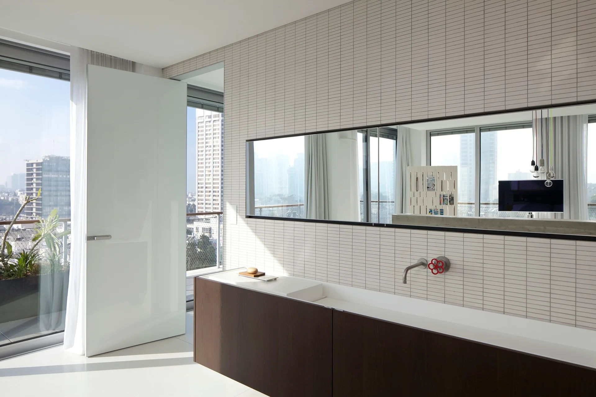 A modern bathroom with a long dark wood vanity, a wide rectangular mirror, and a wall covered in narrow horizontal tiles.