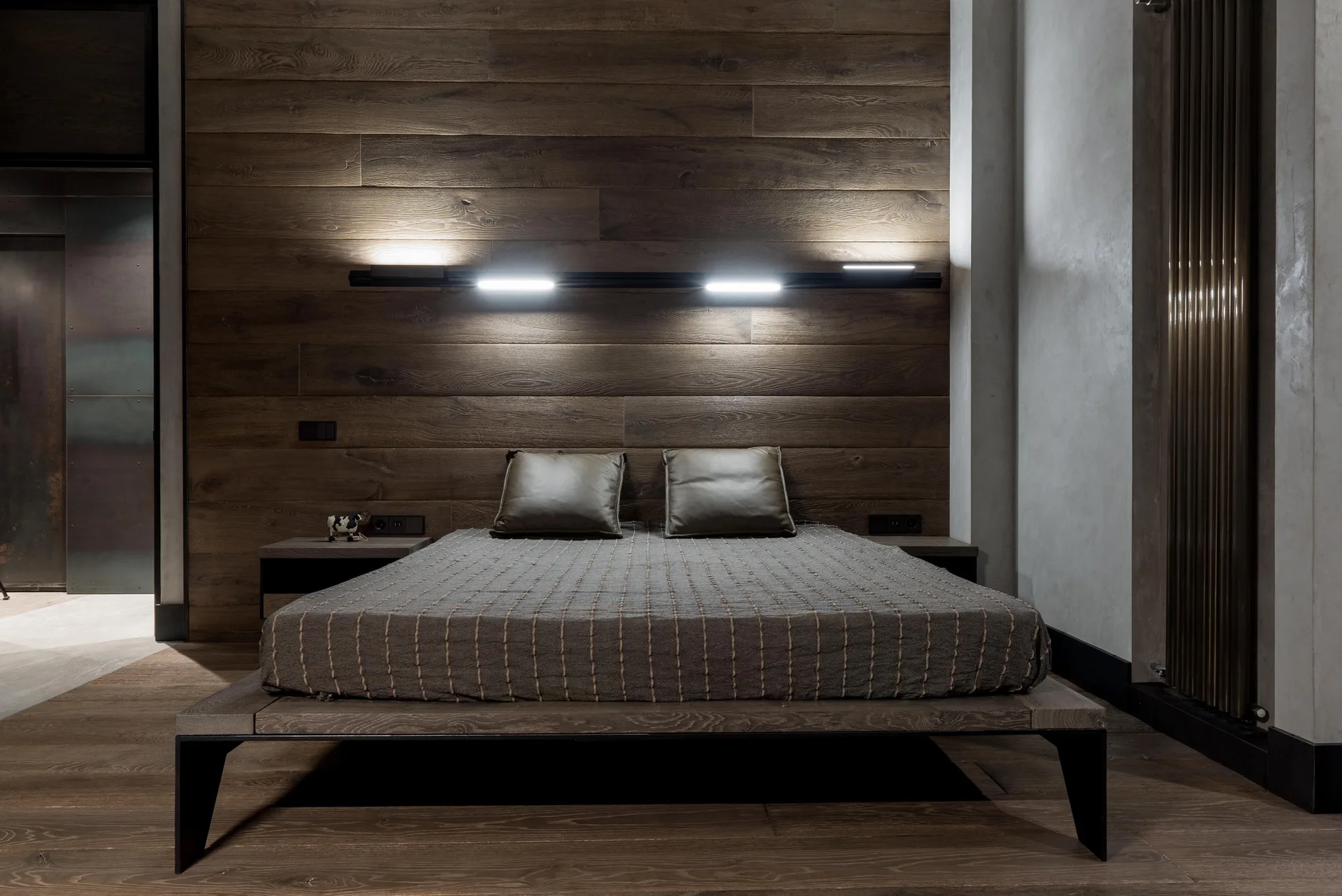 A low wood platform bed rests against a dark brown wood plank accent wall with integrated horizontal linear light strips.