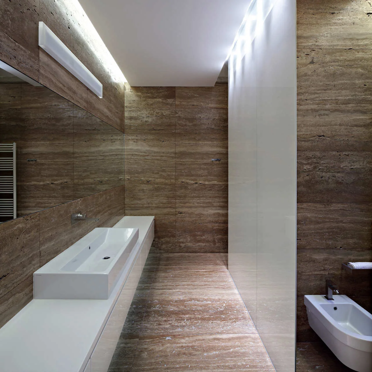 A minimalist bathroom featuring brown travertine stone walls and flooring, a white floating vanity with an integrated sink, and a wall-mounted bidet.