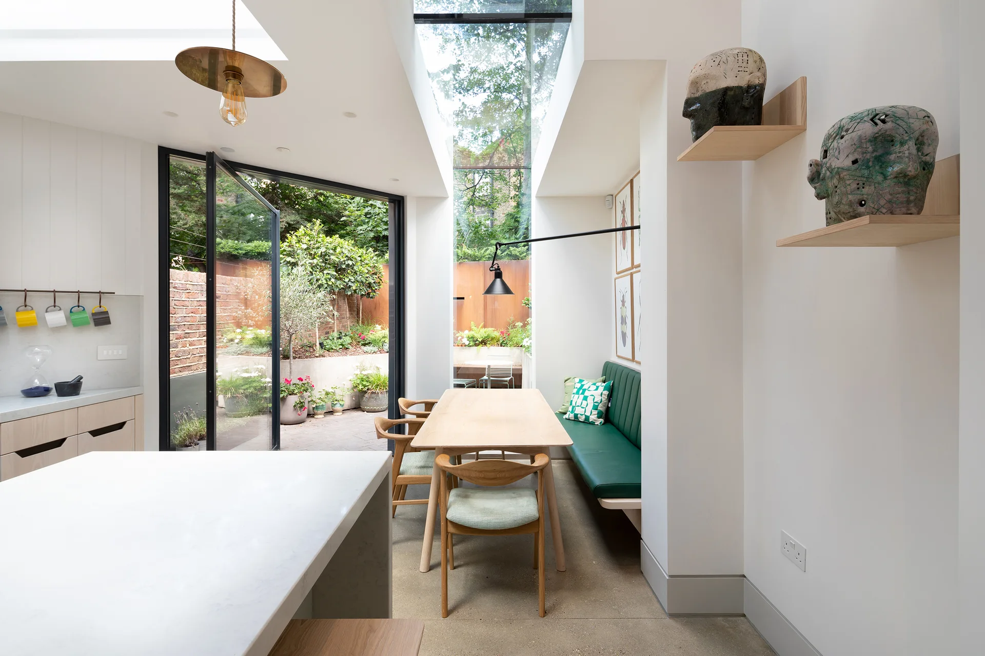 A bright dining area features a light wood table, a green built-in banquette, and large glass doors opening to an outdoor courtyard.
