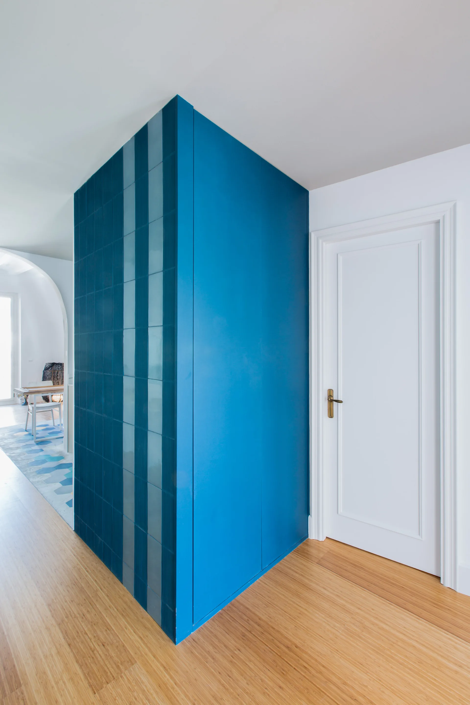 A hallway transition features a bright blue corner wall with square ceramic tiles next to a white paneled door and light wood floors.