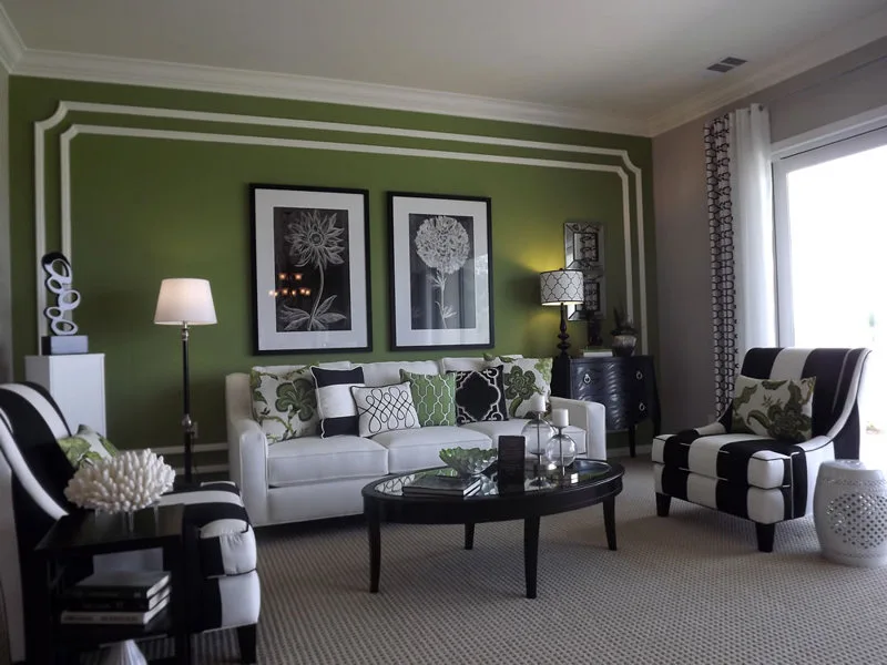 A transitional living room features a green wall with white molding, a white sofa, and two black-and-white striped armchairs.