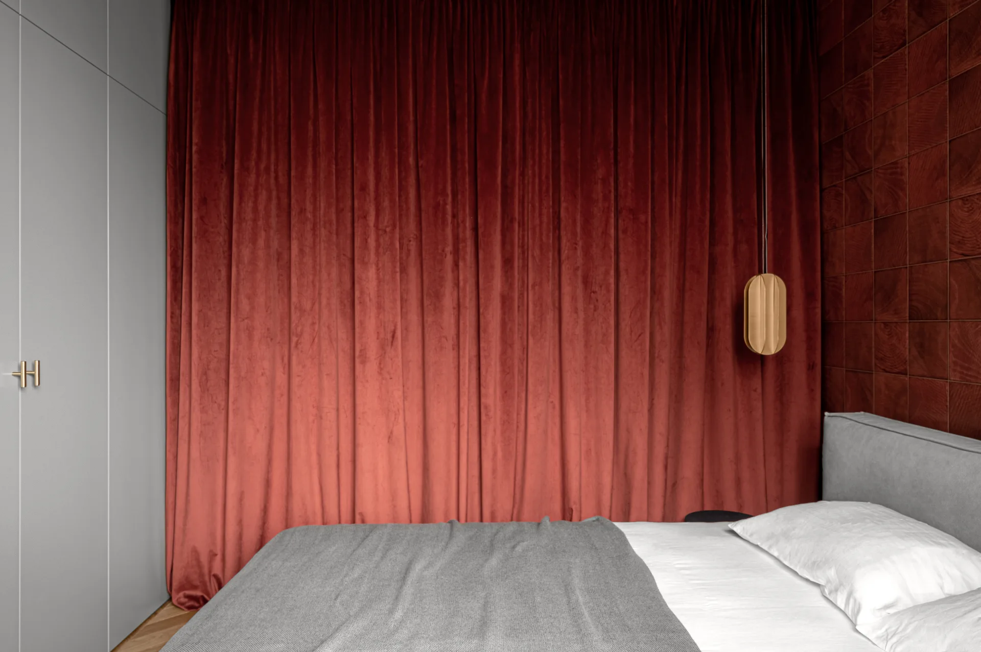 A contemporary bedroom features a grey bed positioned in front of floor-to-ceiling red velvet curtains and gridded dark wood wall paneling.