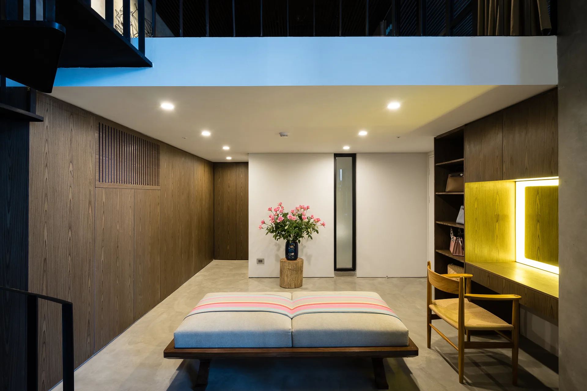 A minimalist entry hall featuring wood-paneled walls, a gray concrete floor, and a large fabric bench with a colorful striped pattern.