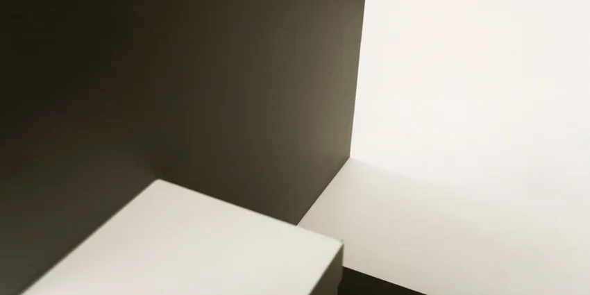 A close-up view of intersecting matte black and white geometric wall surfaces with sharp angles and high-contrast lighting.