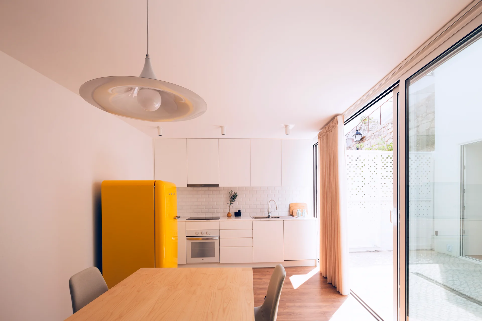 A bright kitchen featuring white cabinets, a yellow retro refrigerator, a wooden dining table, and a sliding glass door opening to a patio.