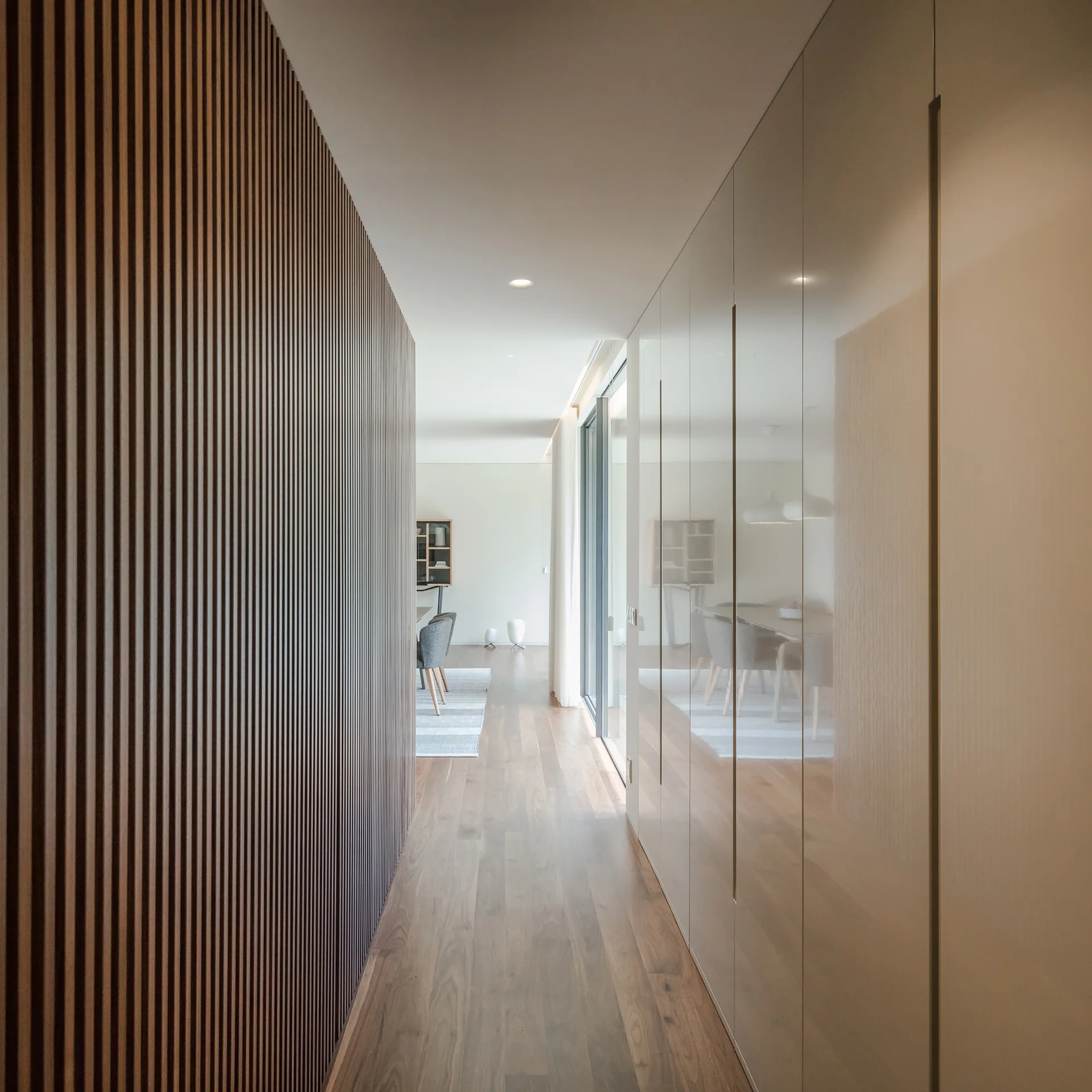 A long contemporary hallway featuring a vertical slatted wood wall on one side and a run of floor-to-ceiling high-gloss cabinets on the other.