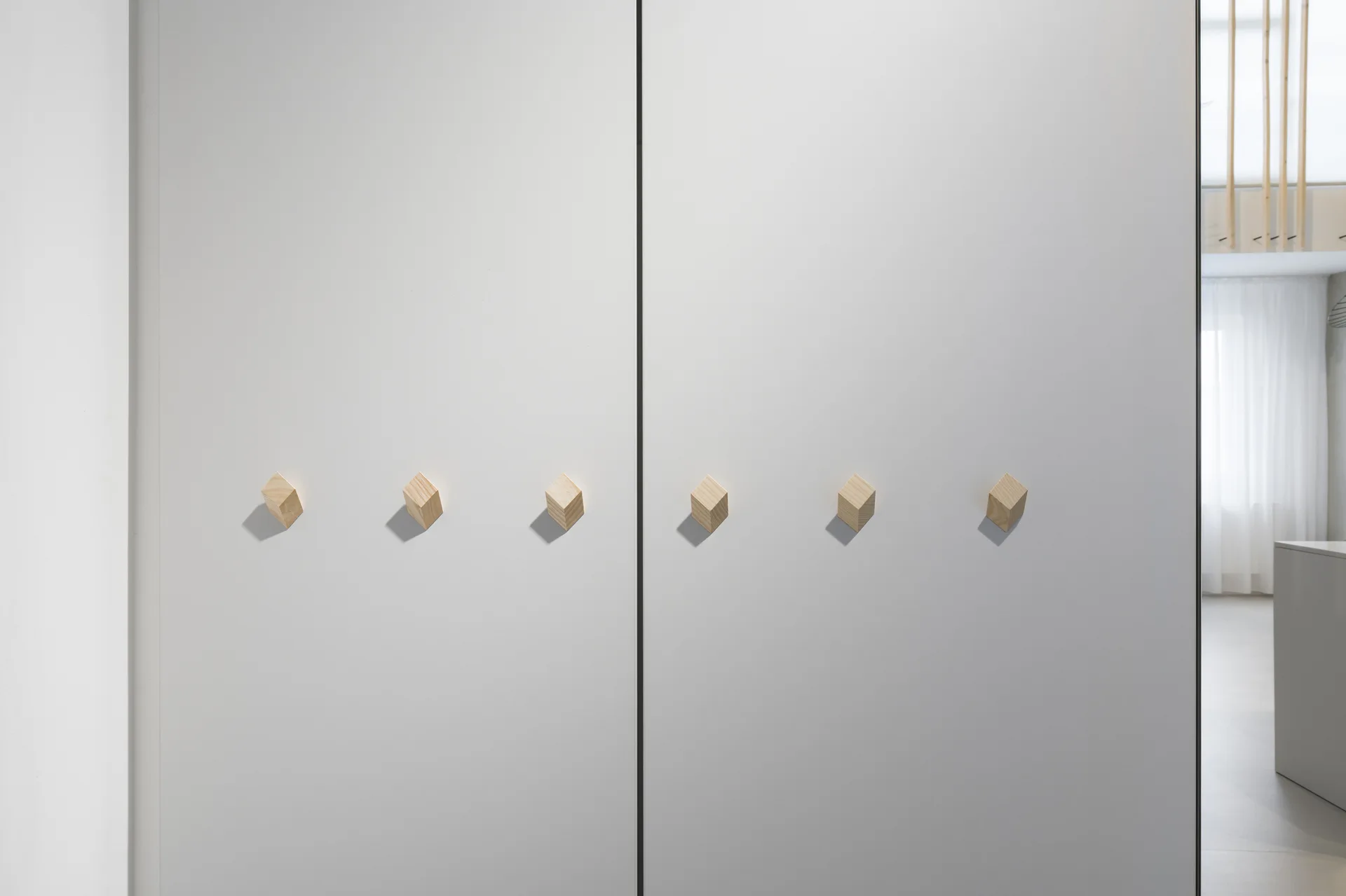 A minimalist white closet with seamless doors featuring six geometric light wood cube handles aligned horizontally.