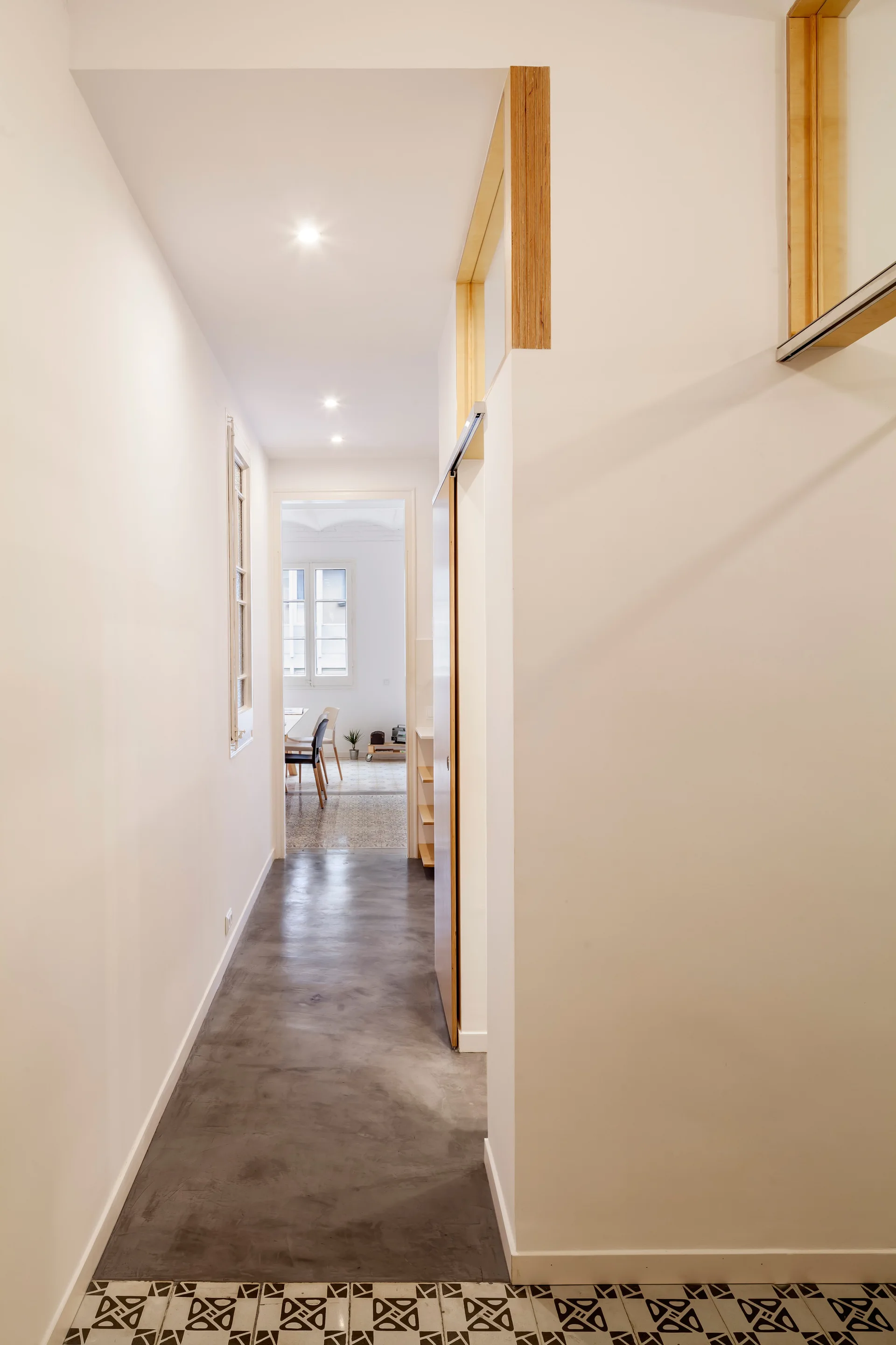 A long white hallway features matte grey concrete flooring that transitions to black and white geometric tiles in the foreground.