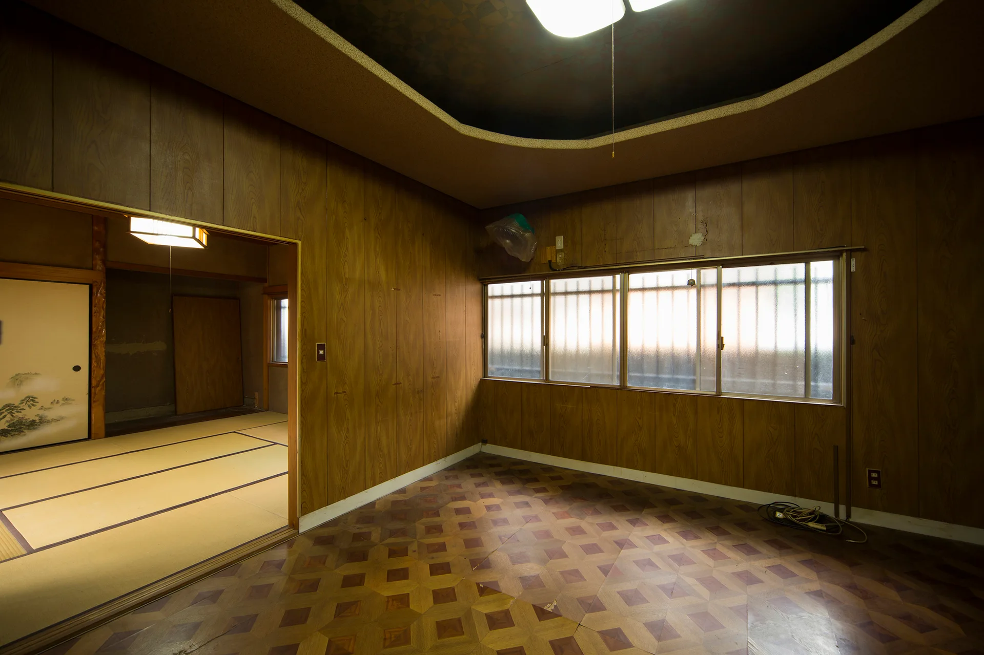 A room featuring vertical wood-paneled walls, geometric pattern flooring, a coved ceiling, and an open doorway to a traditional tatami mat room.