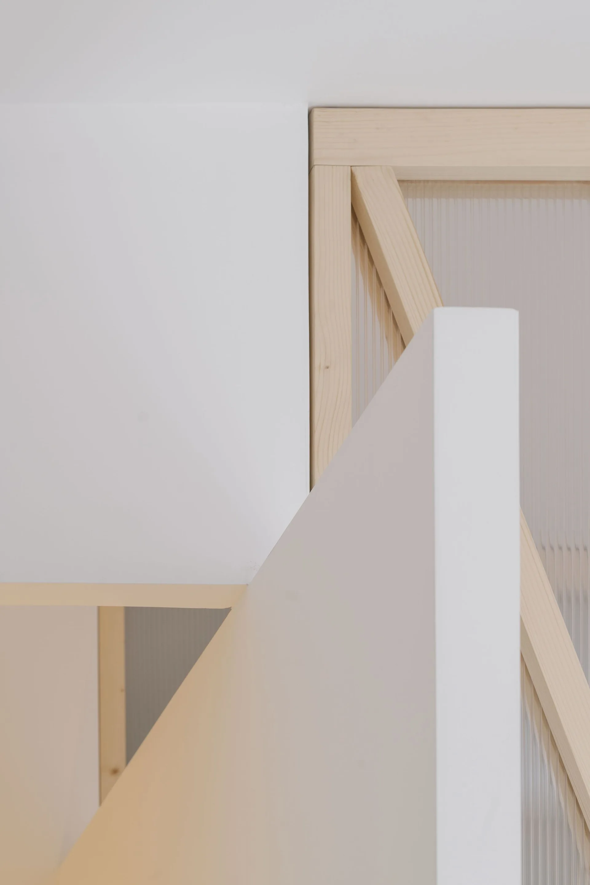Close-up of a minimalist staircase featuring light wood framing, a translucent fluted panel, and clean white walls.