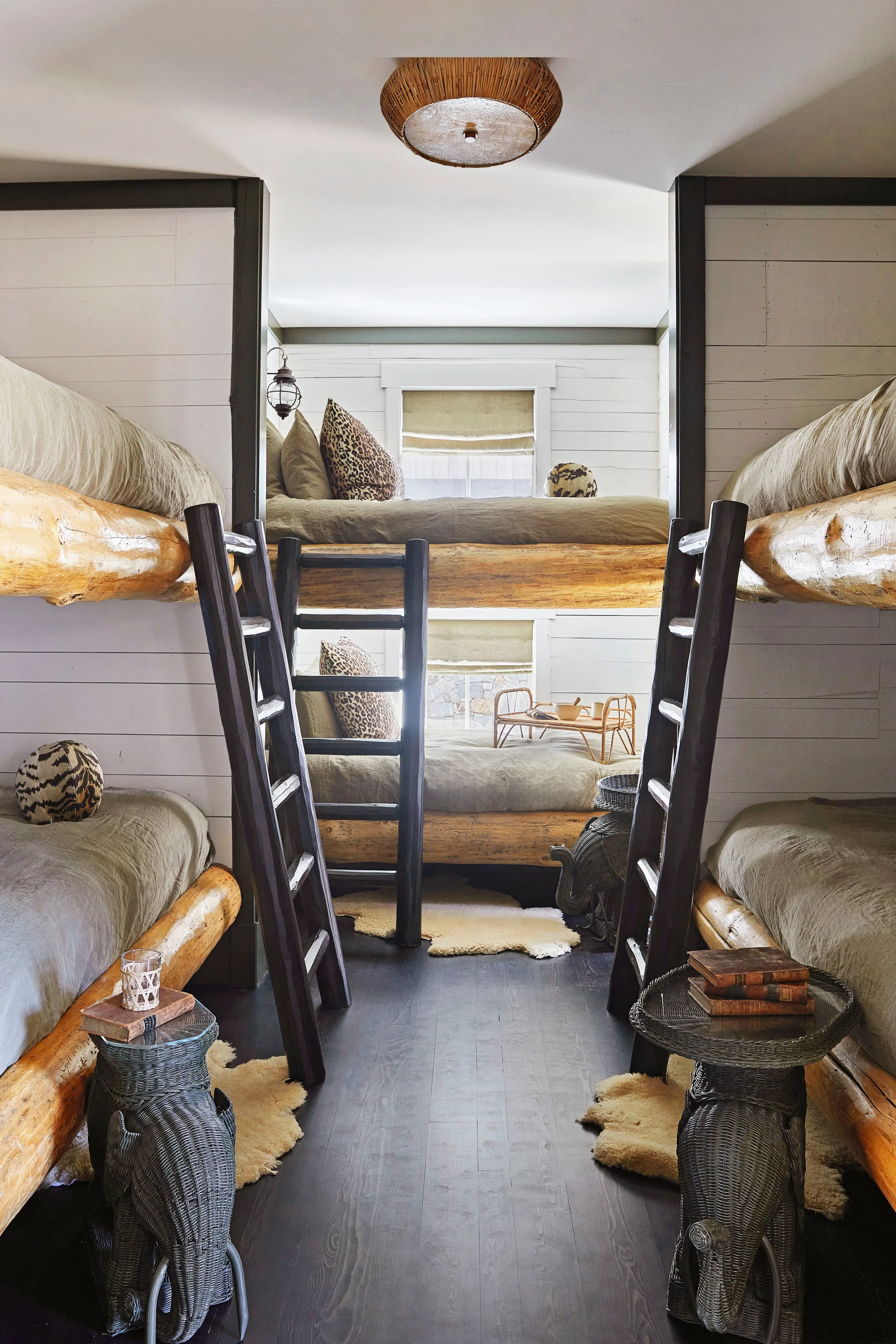 A rustic shared bedroom features multiple built-in log bunk beds, dark wood ladders, white plank walls, and unique elephant-shaped side tables.