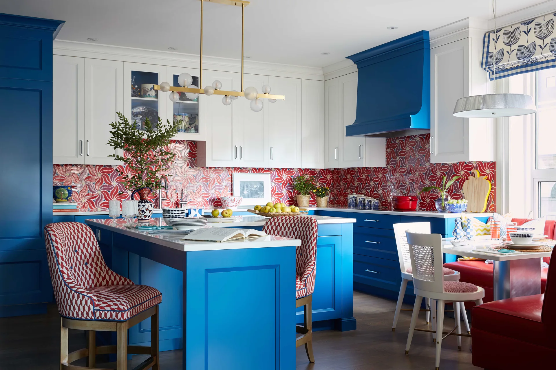 A colorful kitchen with blue lower cabinetry, a white countertop island, and a red and white patterned tile backsplash.