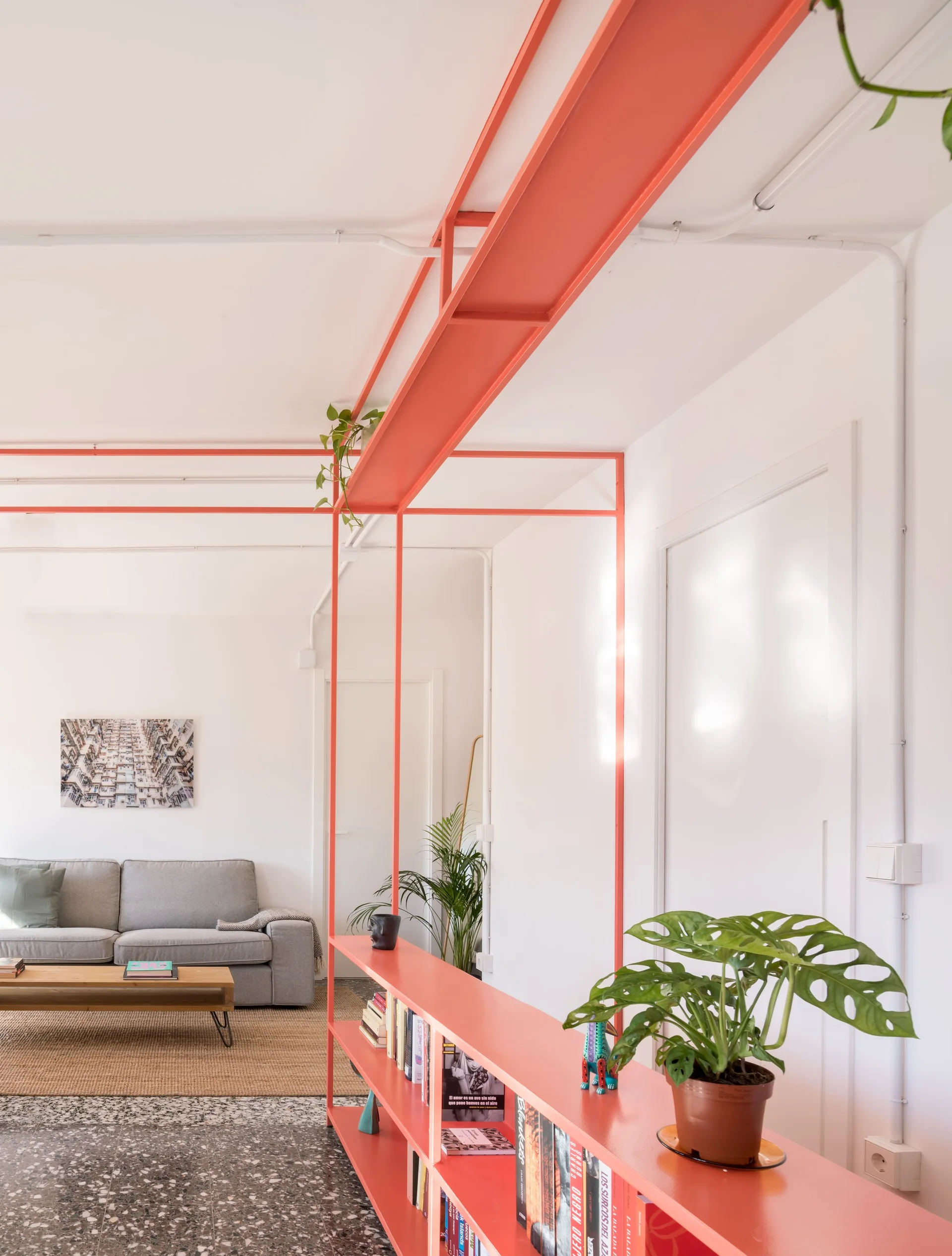 A gray sofa and low wood coffee table sit on a woven rug near a bright red metal shelving unit and speckled terrazzo flooring.