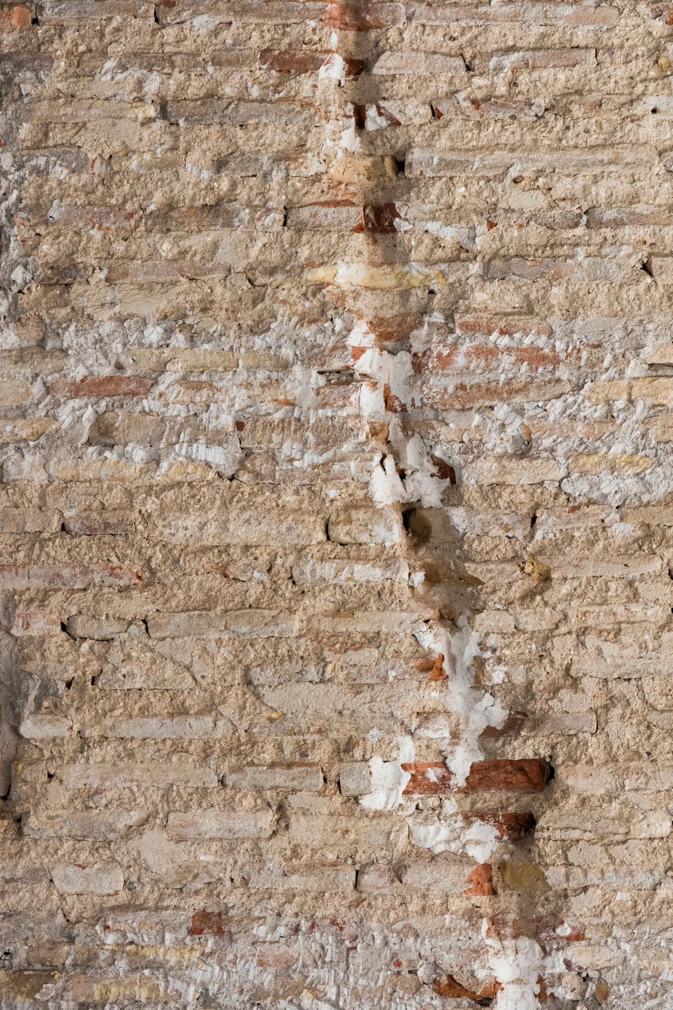 A close-up view of an aged, weathered brick wall showing rough terracotta and beige bricks with uneven, cracked white mortar joints.