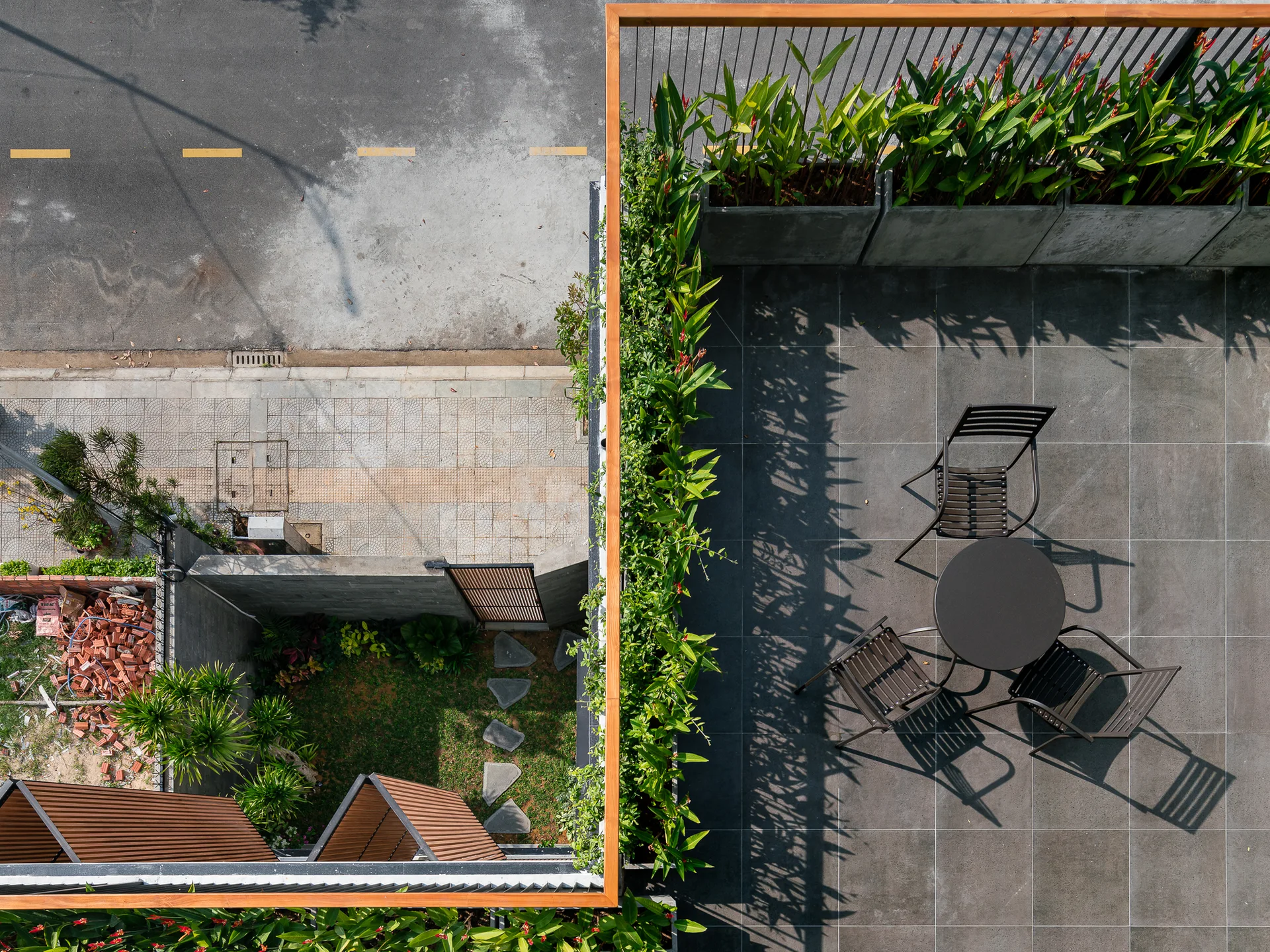 An aerial view of a dark grey tiled terrace featuring a black dining set and long concrete planters filled with lush green plants.