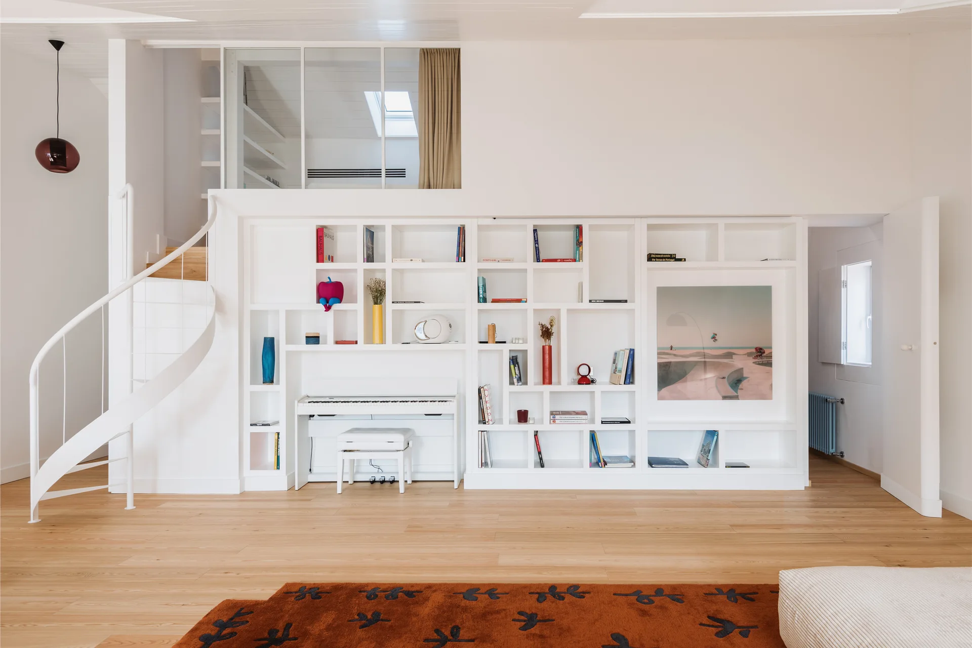 A large white built-in shelving unit with an integrated keyboard sits next to a metal spiral staircase leading to a loft mezzanine.