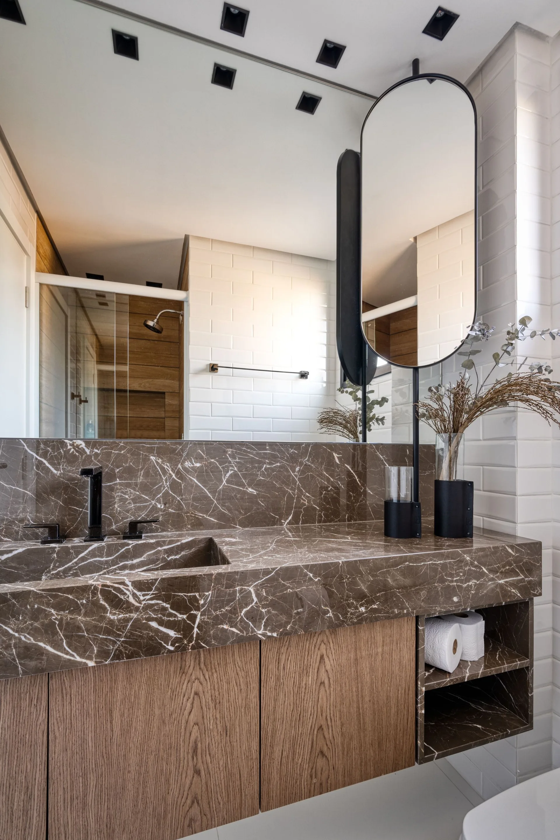 A modern bathroom vanity featuring a veined brown marble countertop with an integrated sink, wood-toned cabinets, and an oval black-framed mirror.