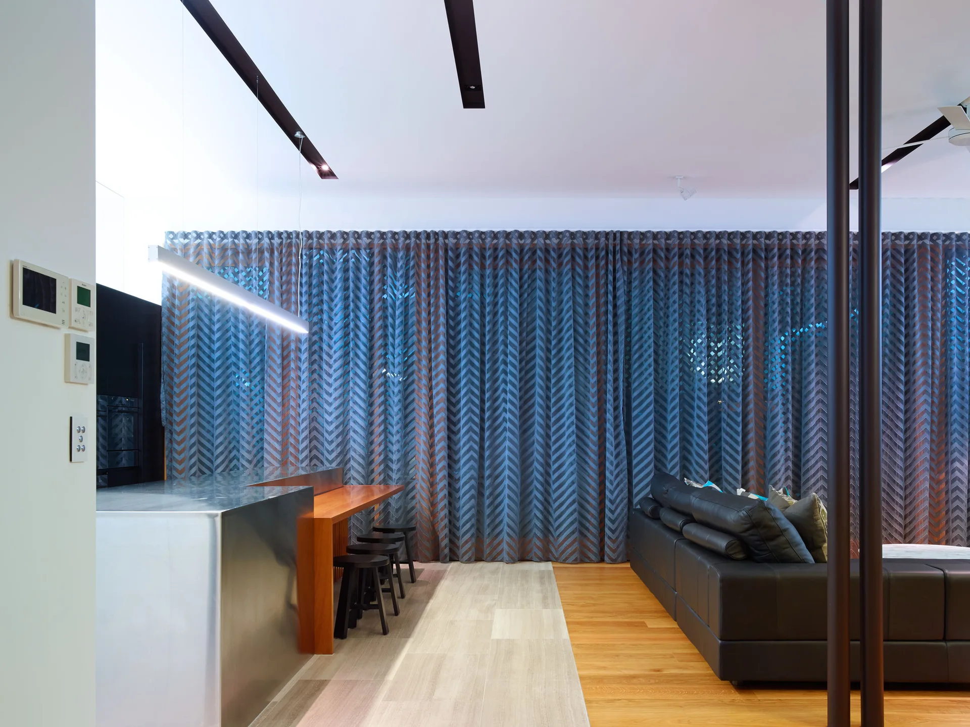 A modern living area with a dark leather sofa, stainless steel kitchen island, and full-length chevron curtains.