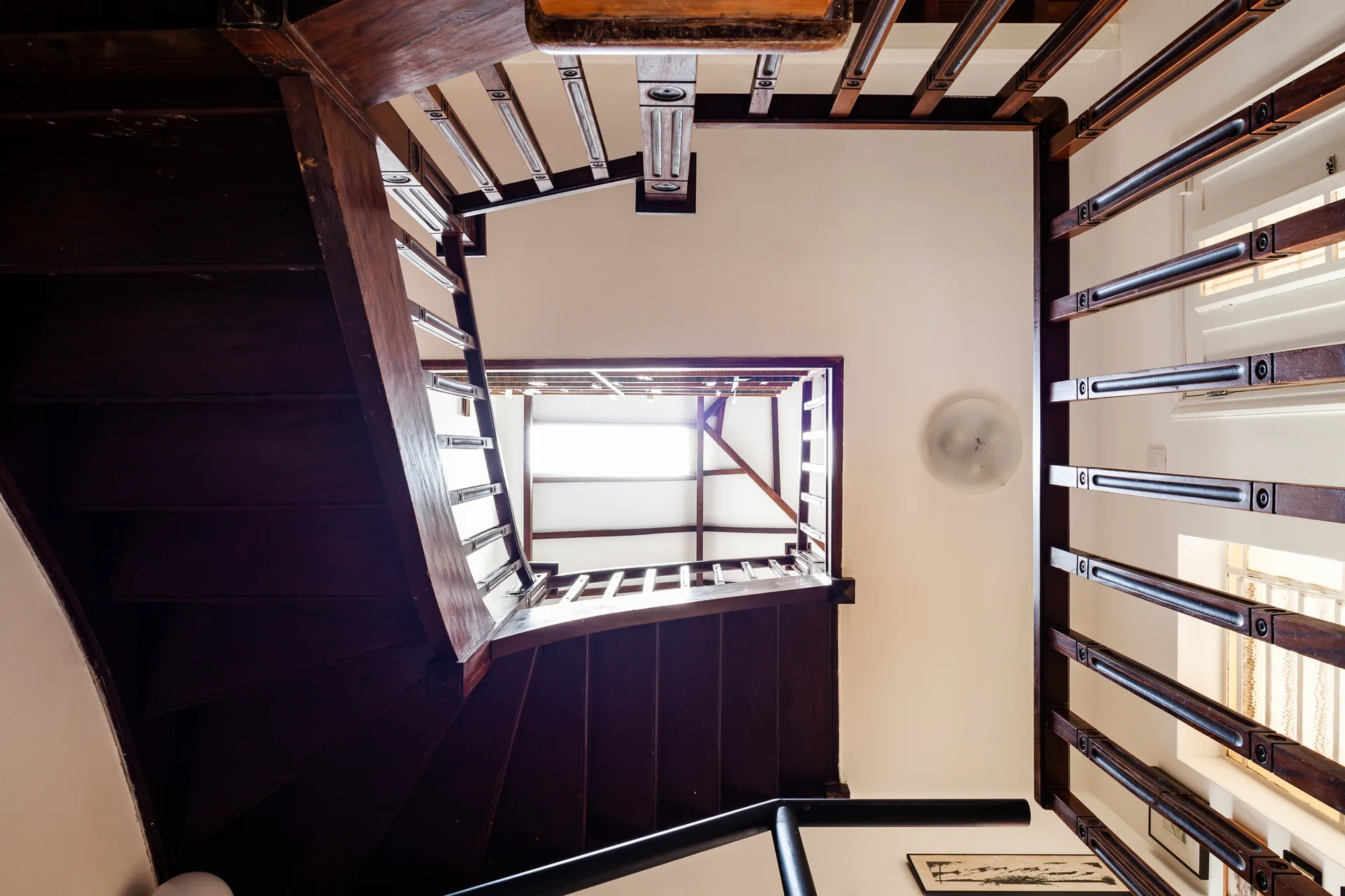 A low-angle upward view of a multi-level dark wood staircase with decorative balusters, white walls, and a bright central skylight.