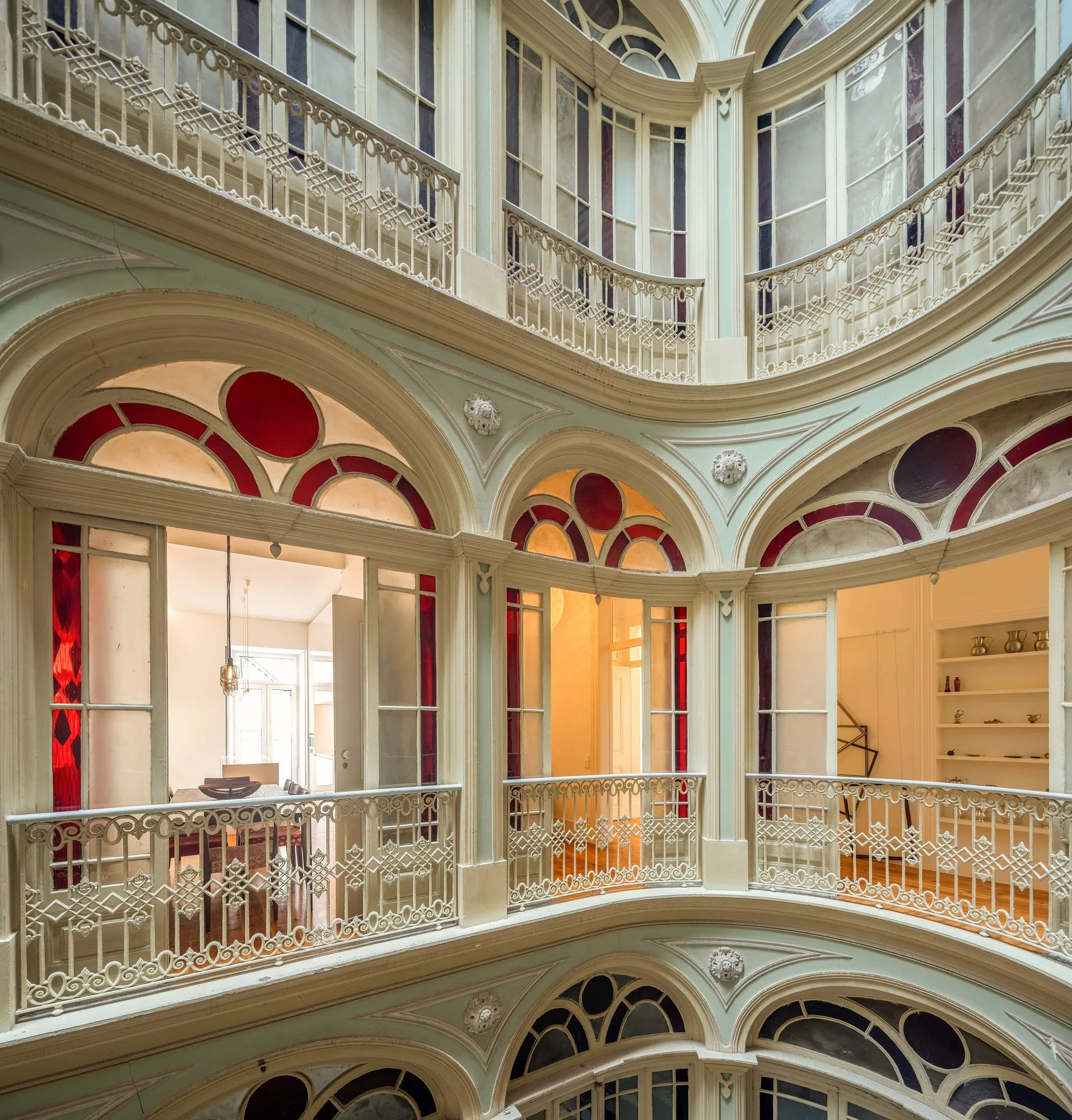 A multi-level interior atrium features curved mint green corridors with ornate white iron railings and arched doorways featuring red stained glass.