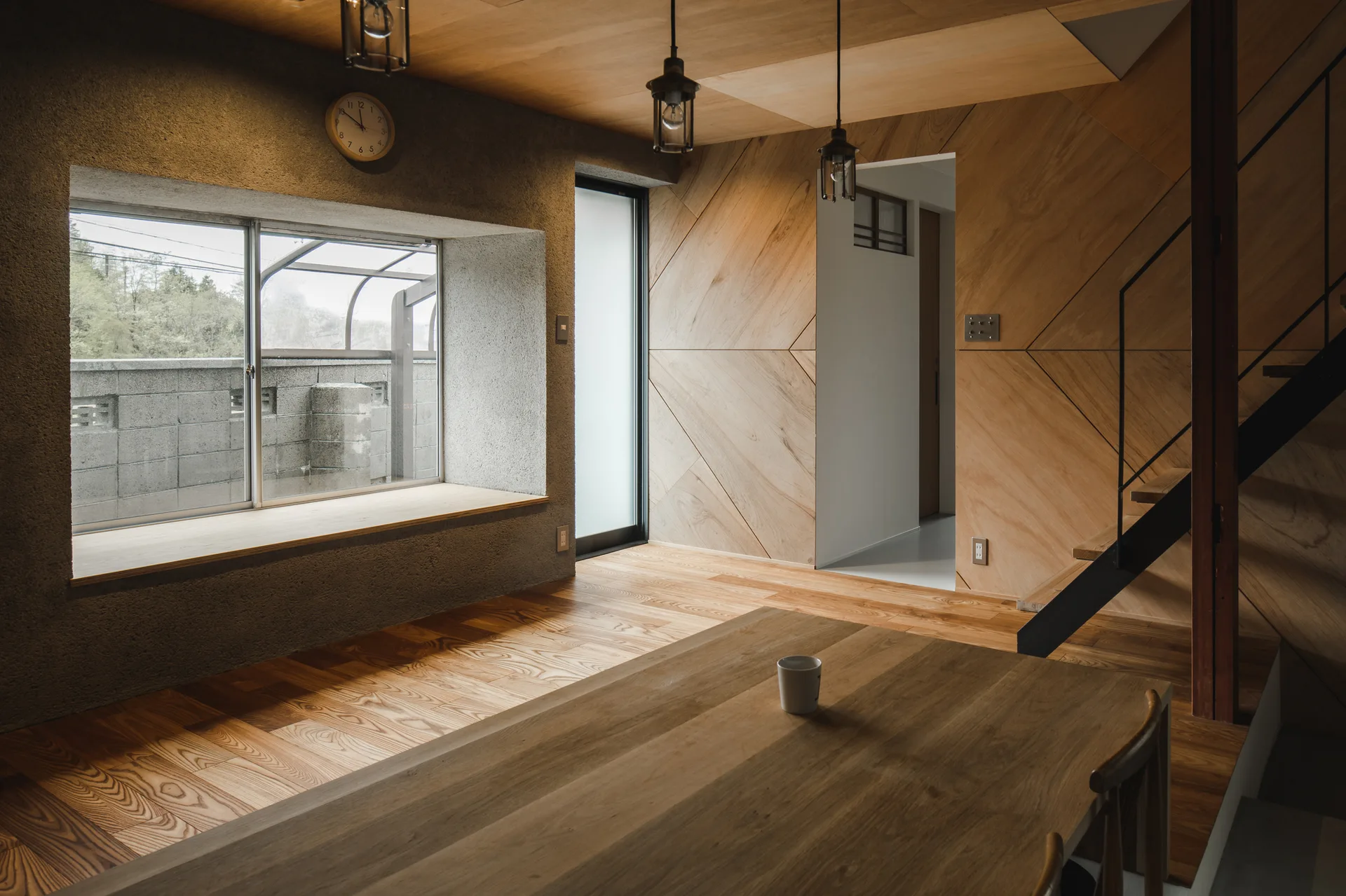 A modern residential interior featuring diagonal wood wall paneling, a concrete wall with a recessed window bench, and a wooden dining table.