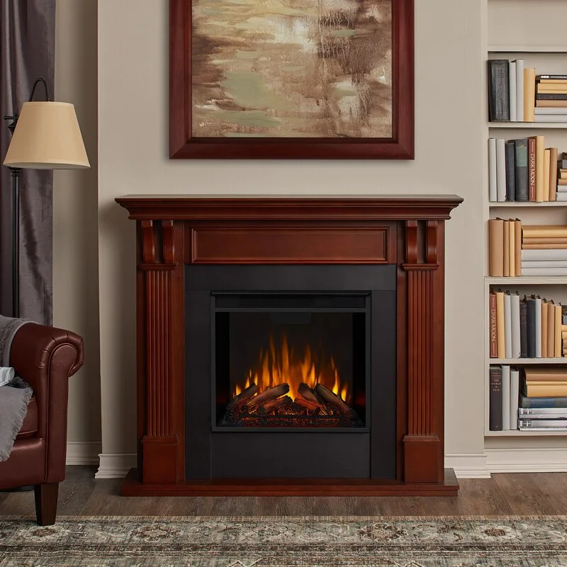 A dark wood fireplace mantel with a glowing electric fire stands against a beige wall next to a built-in bookshelf and a leather armchair.