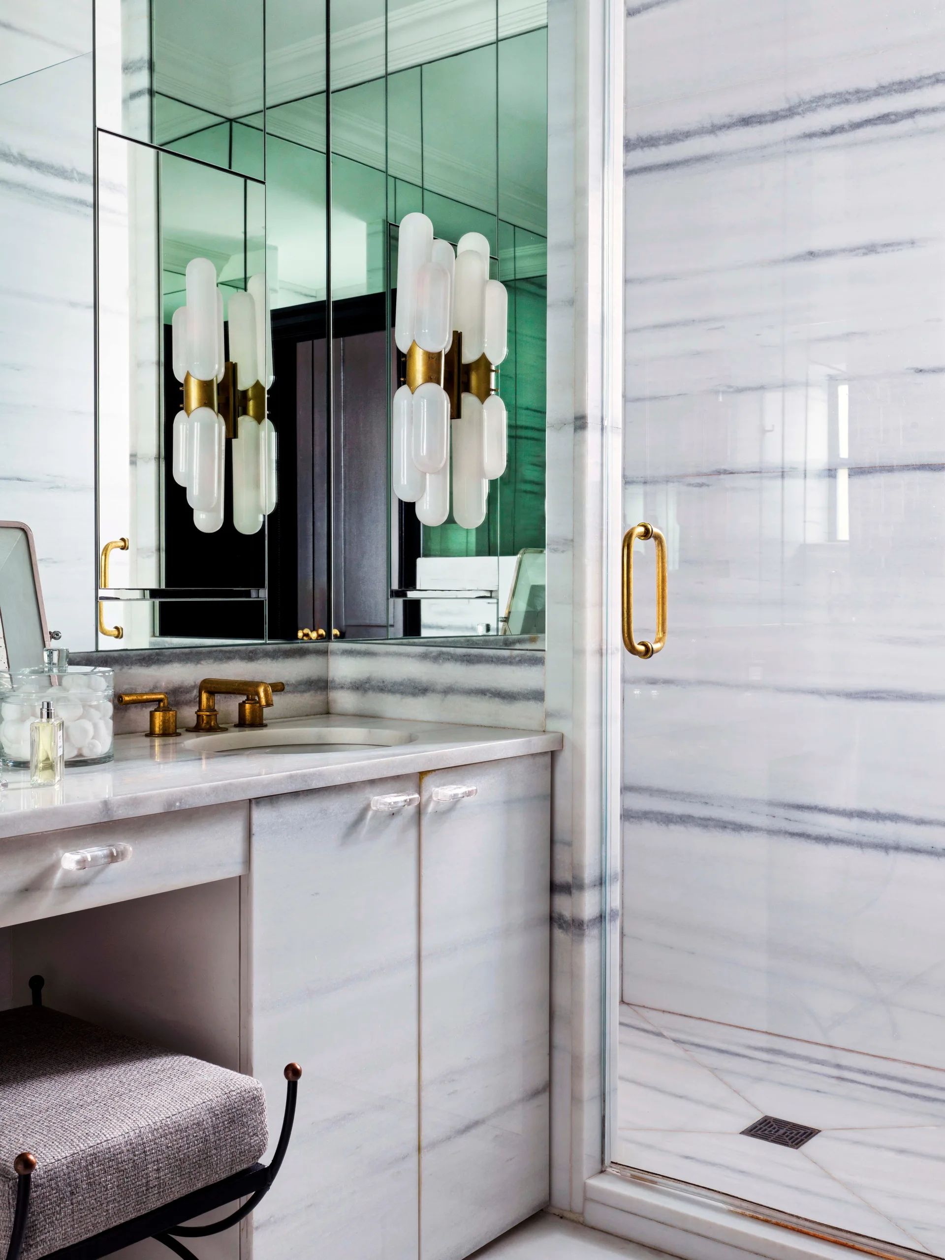 A luxury bathroom features a striped marble vanity and shower wall, a panel mirror, and a frosted glass wall sconce with brass hardware.