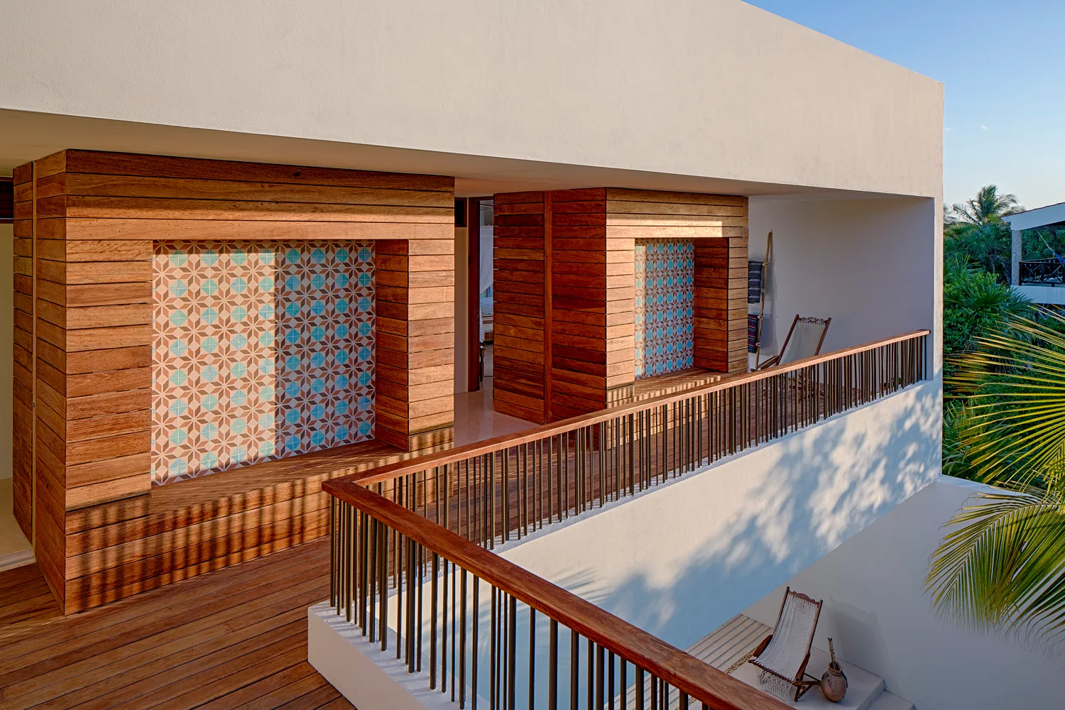 An outdoor wood-decked terrace features wood-clad walls with recessed geometric tile niches, a wooden railing, and folding deck chairs.