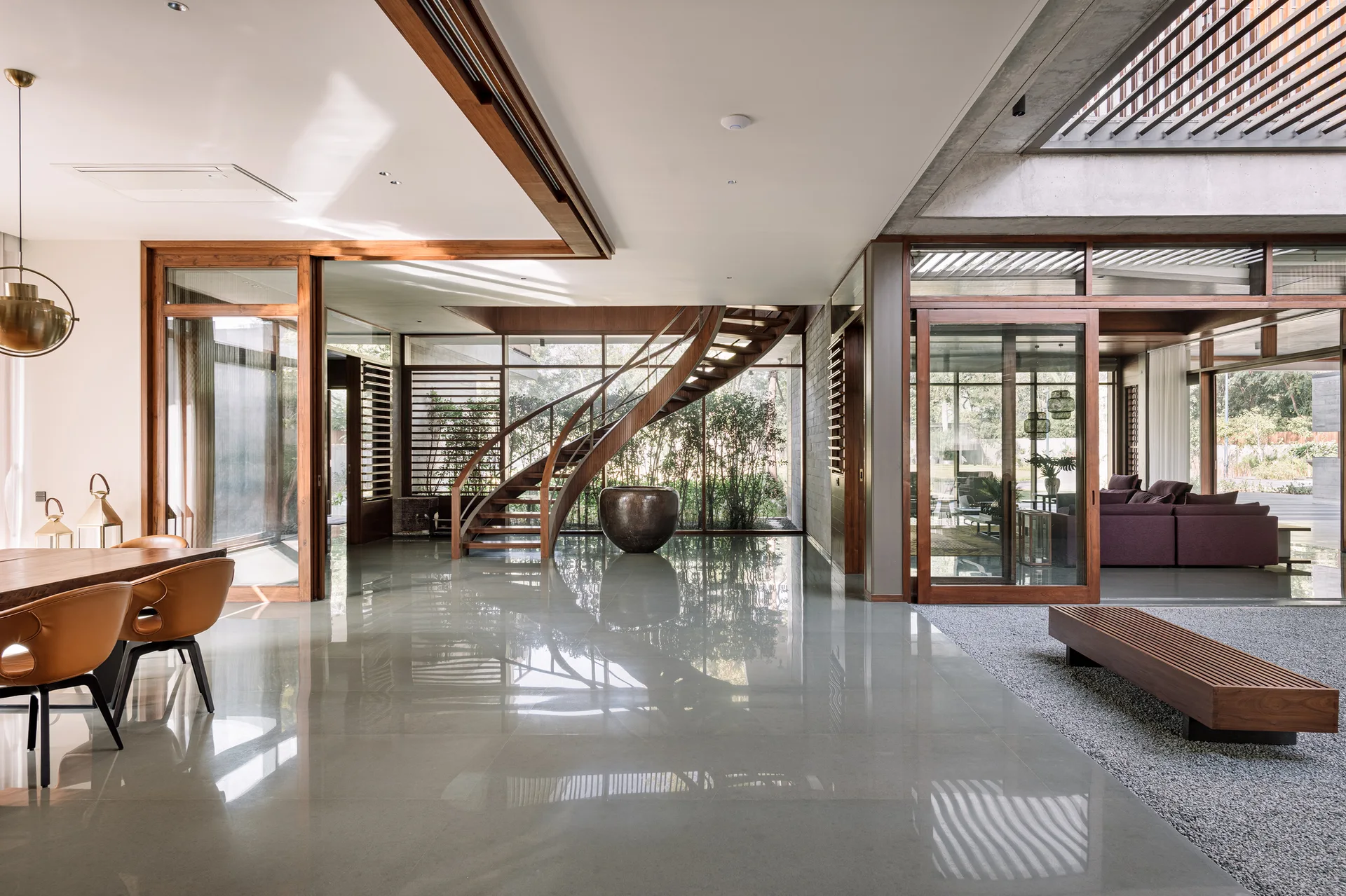 A modern open-concept home interior featuring a curved wooden staircase, polished grey flooring, and wood-framed sliding glass doors.