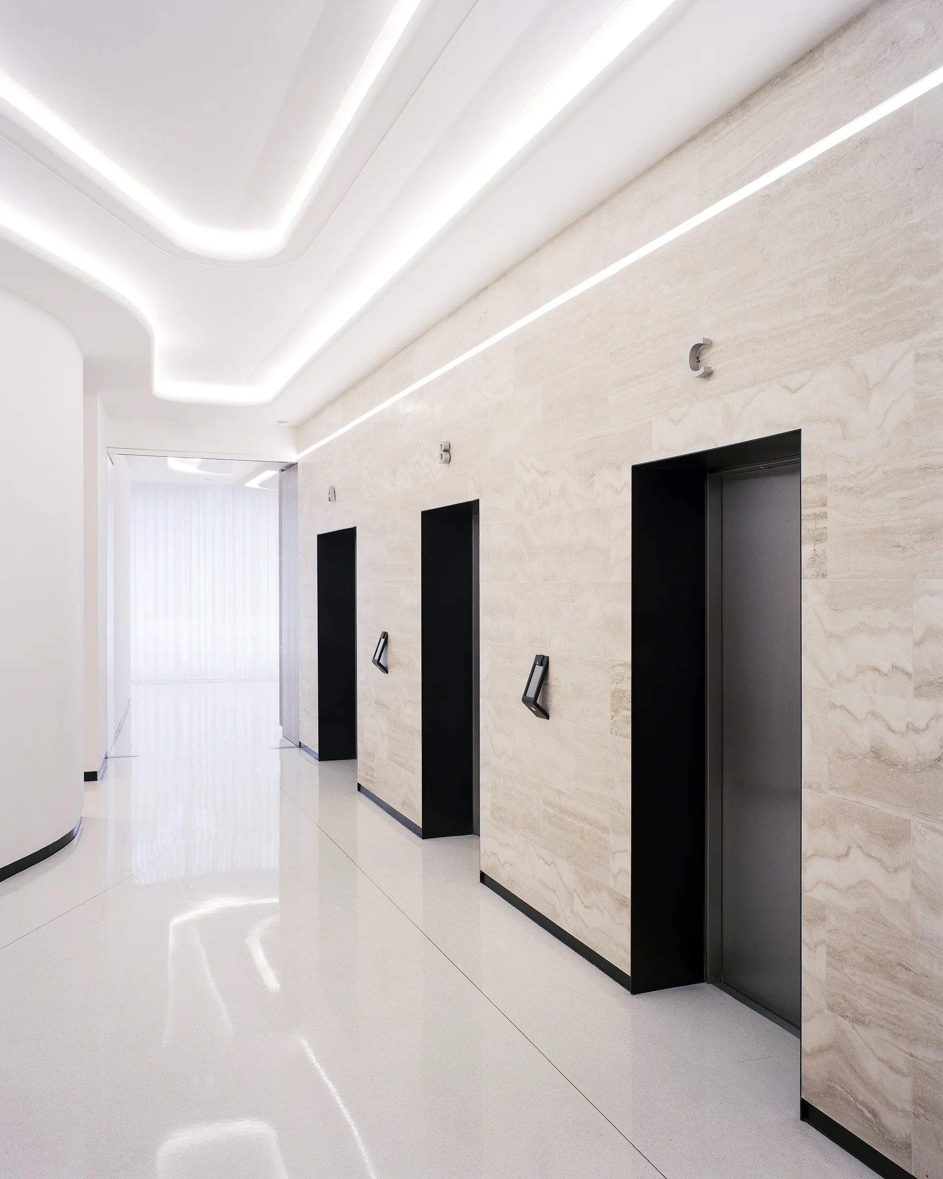 A modern hallway features three black elevator doors set in a beige stone wall with polished white floors and curved ceiling lights.