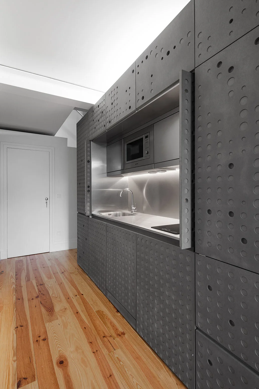 Dark gray perforated kitchen cabinets feature circular cutouts and a recessed stainless steel workstation with a built-in microwave and sink.