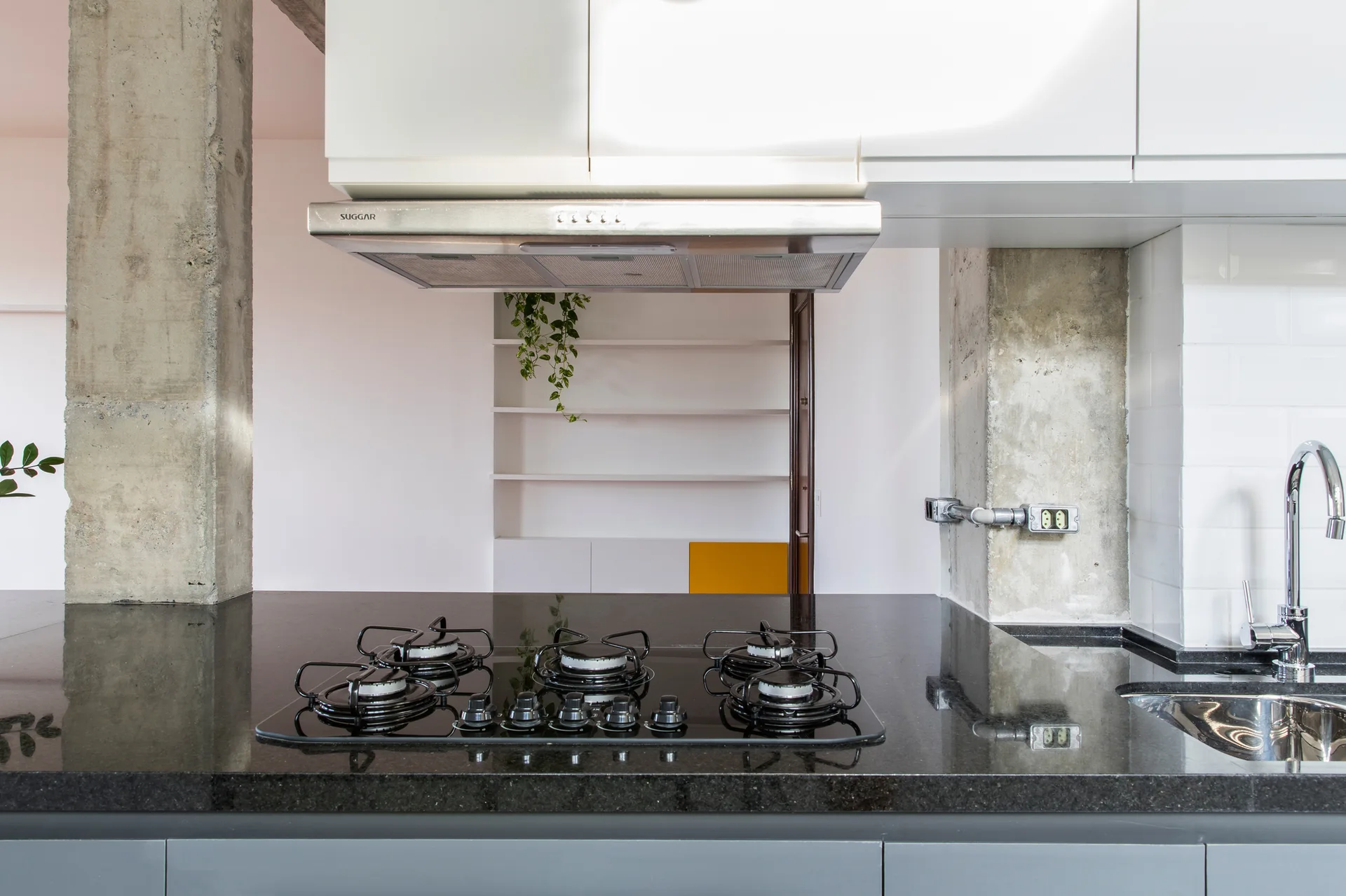 A modern kitchen featuring a black gas cooktop on a dark granite countertop flanked by exposed concrete columns and white upper cabinets.