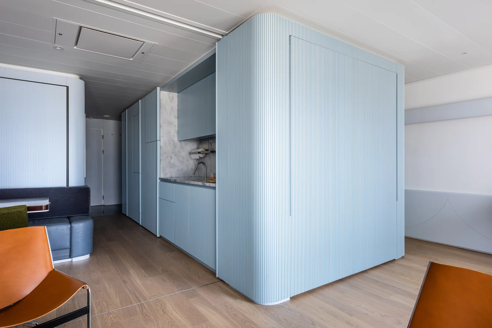 A modern kitchen features a central curved unit clad in light blue fluted paneling, complete with integrated cabinetry, a sink, and wood flooring.
