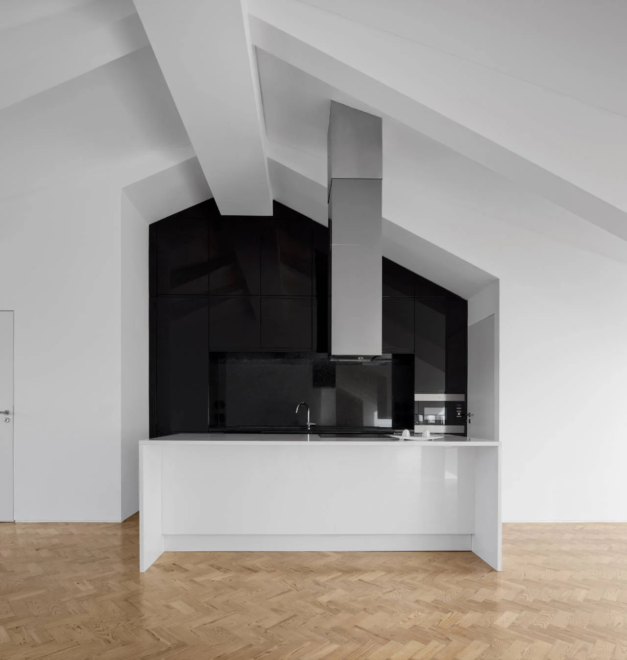 A modern kitchen featuring a white island, glossy black cabinetry under an angled ceiling with beams, and light wood herringbone flooring.