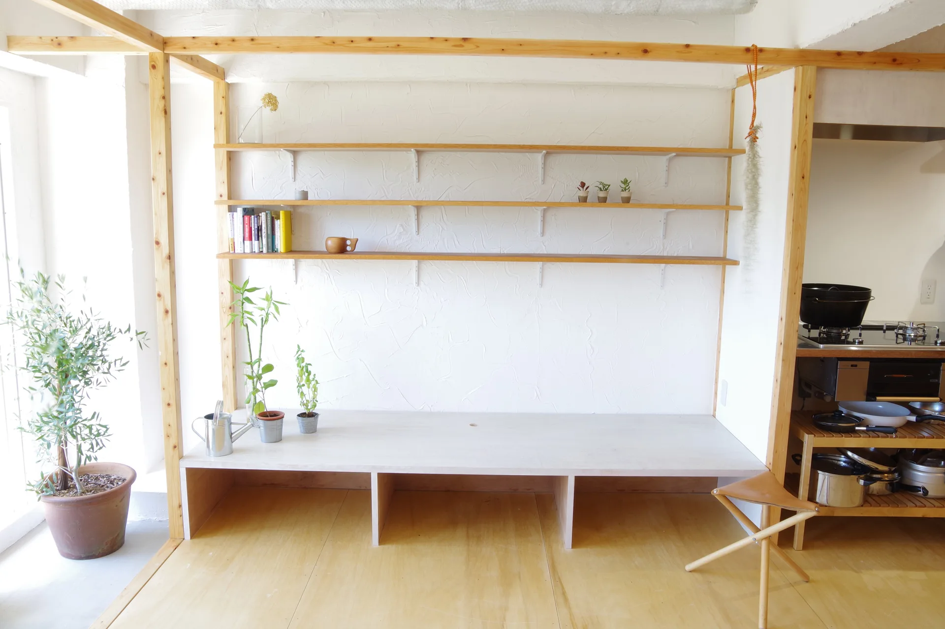 A minimalist room features a custom wood frame enclosing open wooden shelves and a low platform bench against a white textured plaster wall.