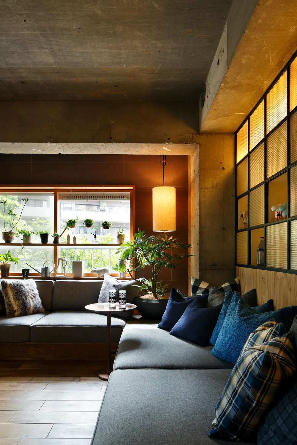 An industrial living room features a grey built-in sofa, an exposed concrete ceiling, and a warm backlit gridded partition screen.