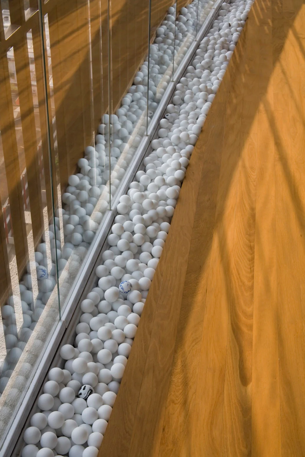 A smooth wooden floor and clear glass railing featuring a narrow built-in floor trough filled with white spheres and patterned balls.