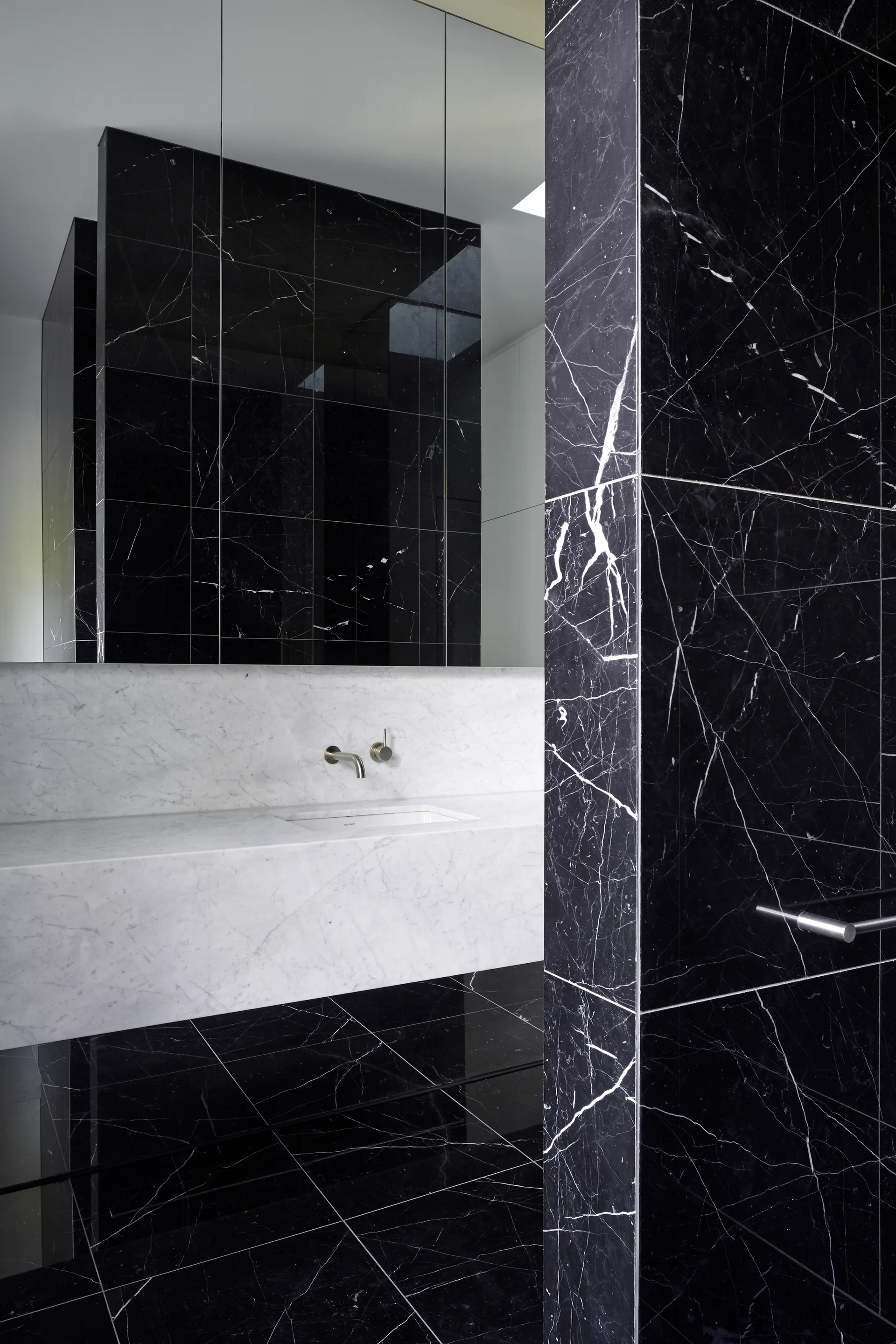 A modern bathroom features a floating white marble vanity with a wall-mounted faucet set against polished black marble wall and floor tiles.