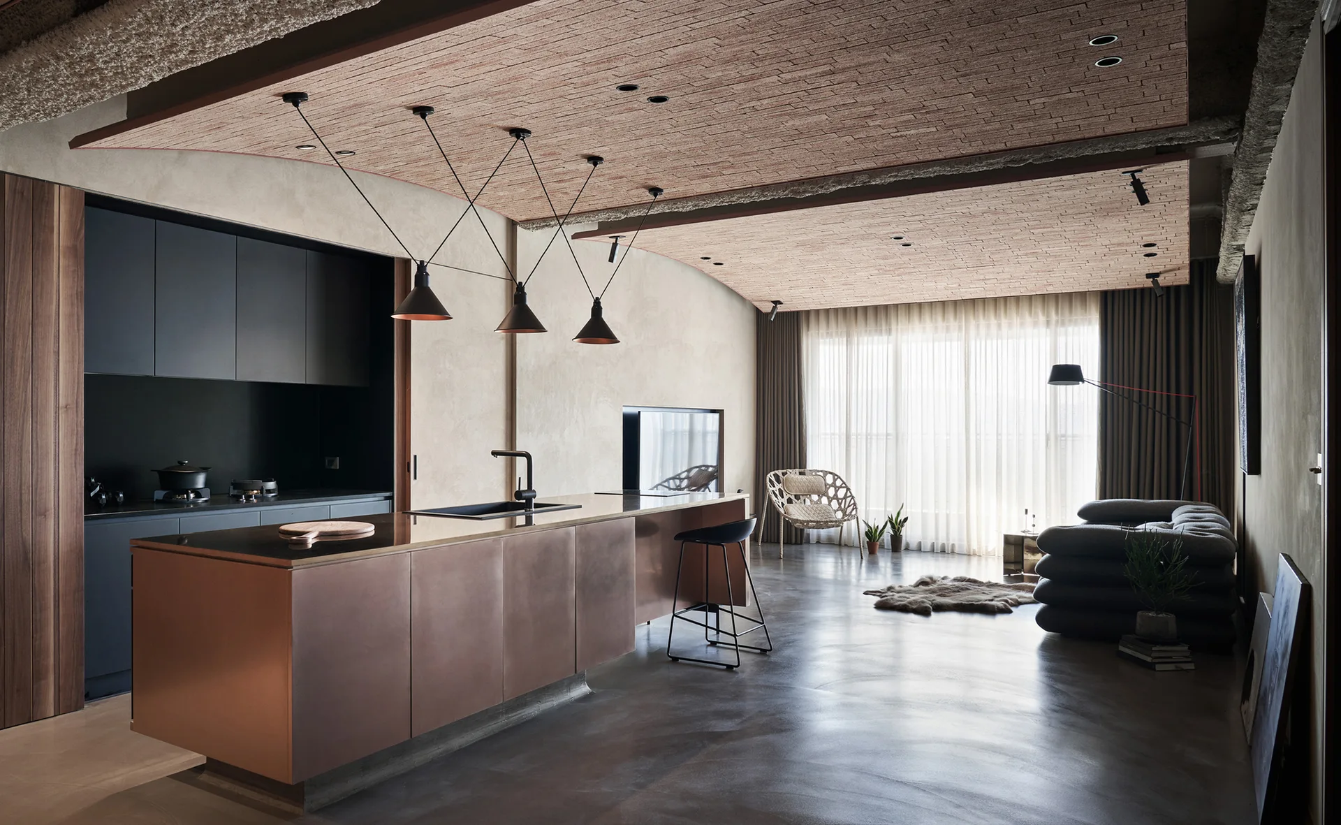 A modern open-concept kitchen features a metallic copper island and dark pendant lights beneath a textured red brick ceiling panel.