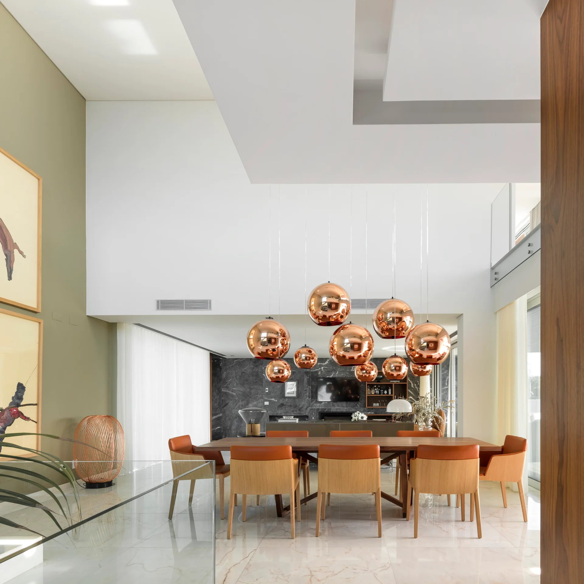 A modern dining room features a long wooden table, orange-upholstered chairs, and a cluster of copper sphere pendant lights.