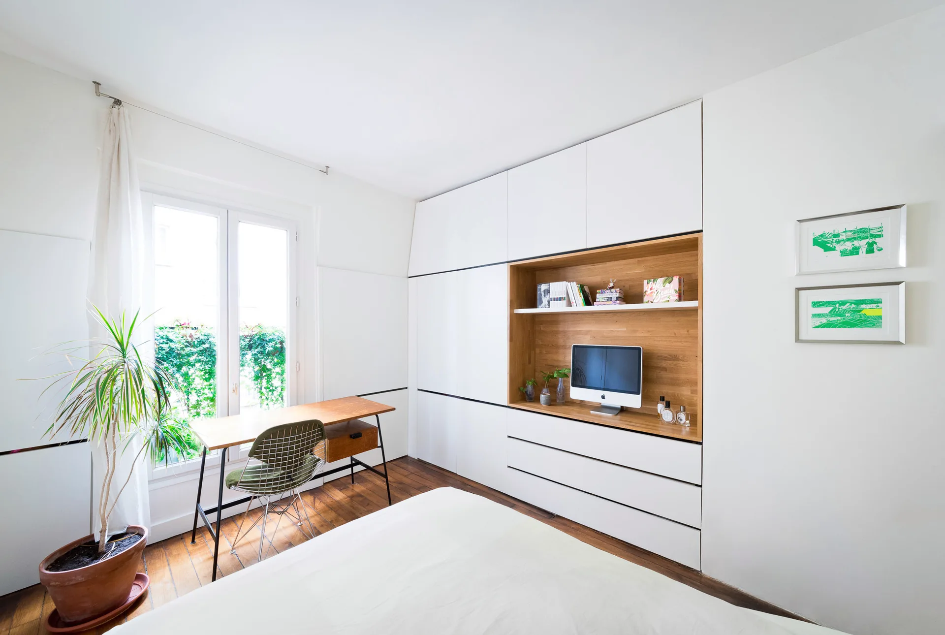 A bedroom features a white built-in wardrobe with an integrated wood alcove, a writing desk by the window, and wood plank flooring.