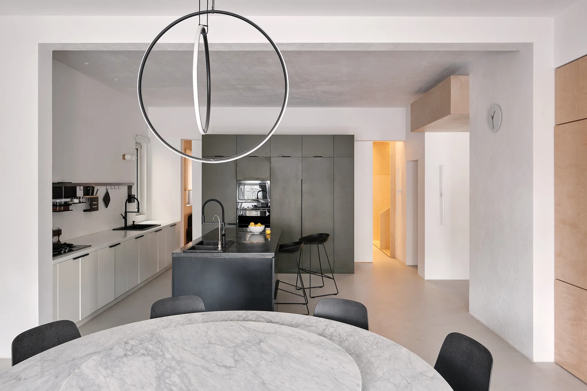 A modern kitchen featuring olive green full-height cabinets, a black island with bar stools, and a marble dining table in the foreground.