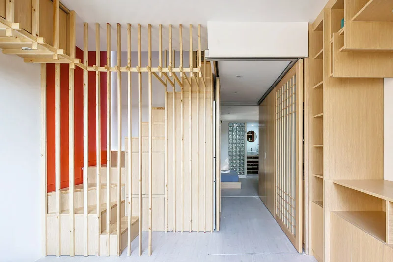 A modern light wood staircase features an integrated vertical slat screen next to a sliding lattice door and built-in shelving.