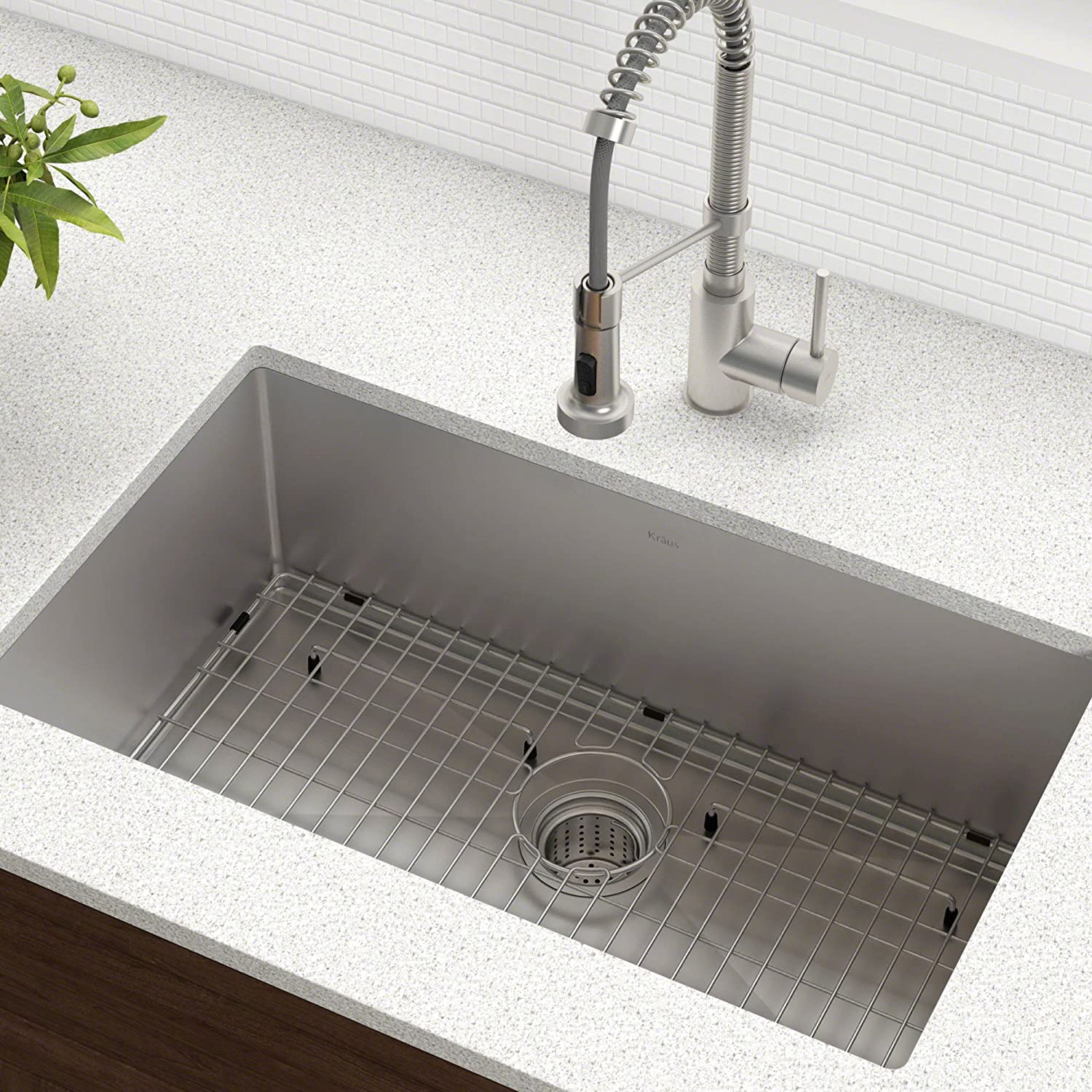 An undermount stainless steel kitchen sink features a protective metal bottom grid and a tall brushed metal spring-neck faucet on a speckled countertop.