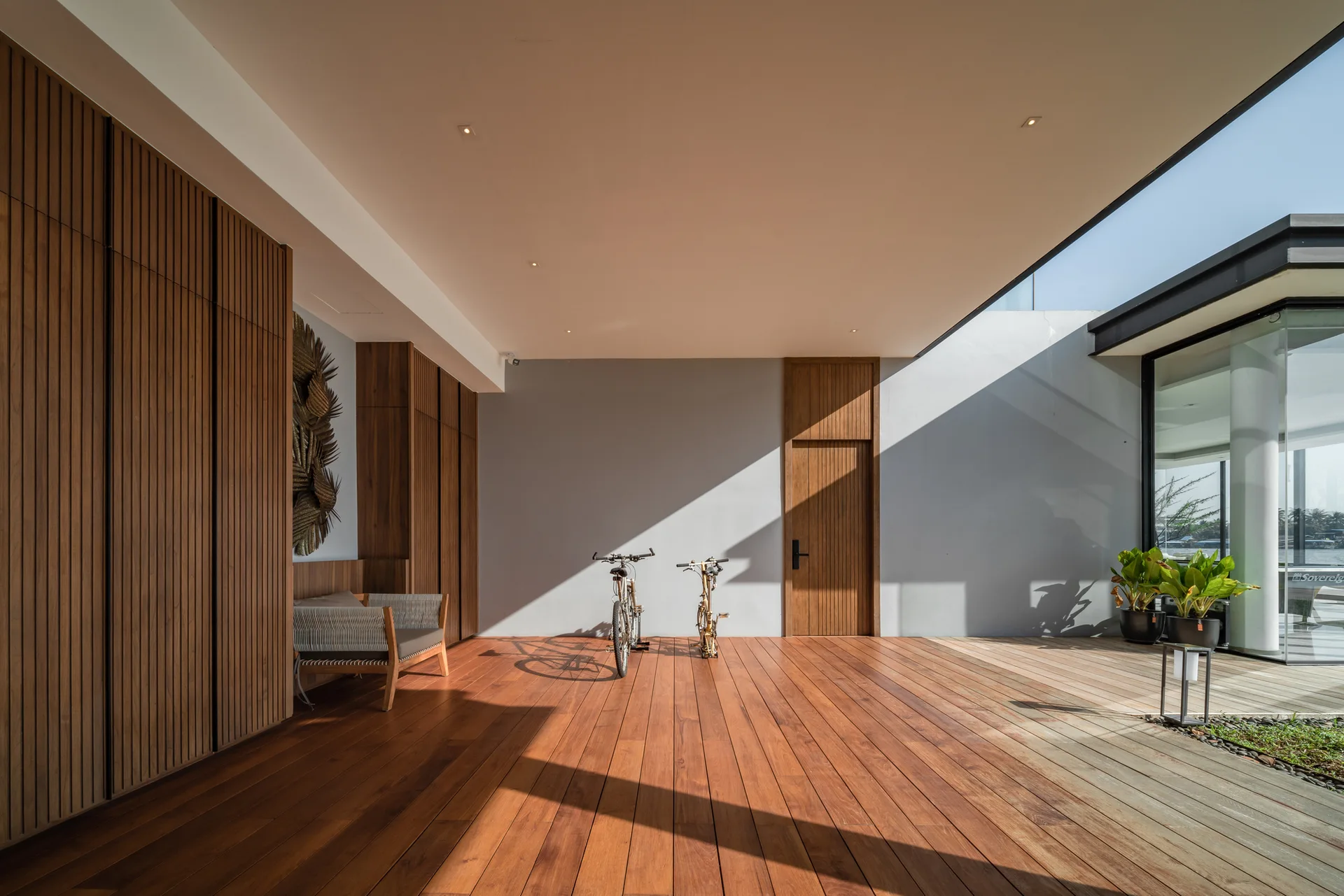 A covered outdoor terrace with wood plank flooring, matching vertical slatted wood storage cabinets, a wood door, and two parked bicycles.